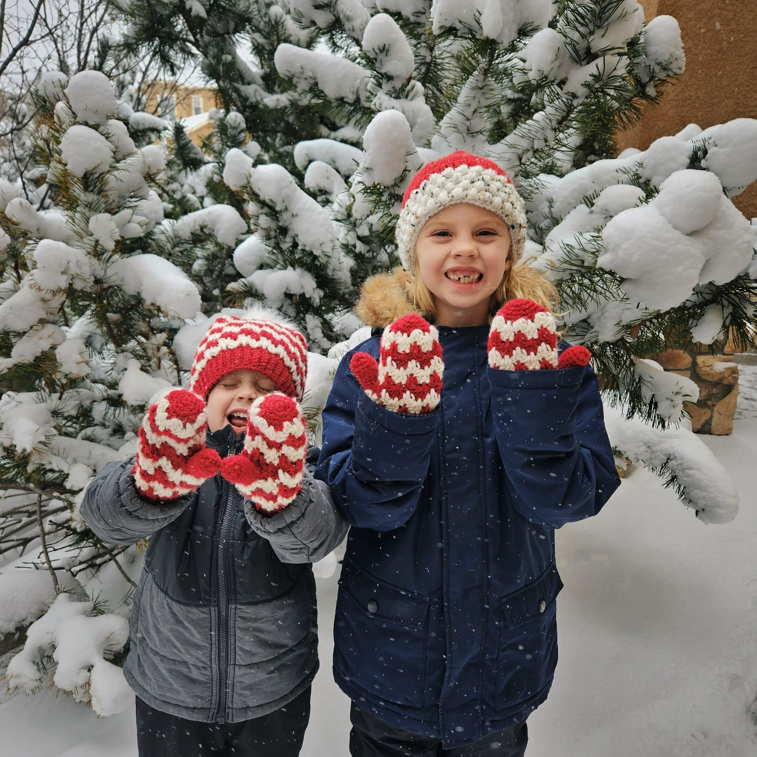 The candy cane mittens crochet pattern being worn in a snowy wonderland