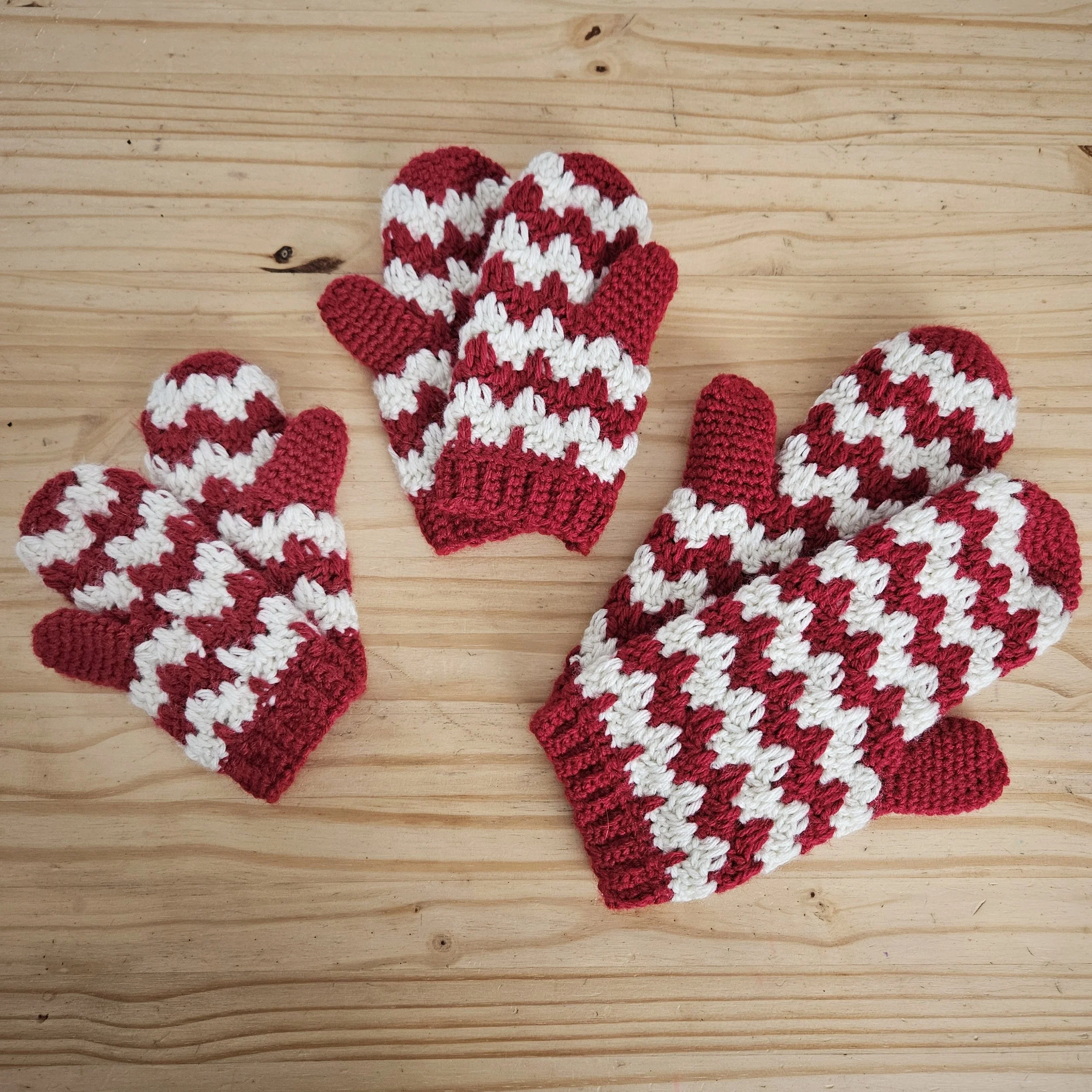 hand crocheted candy cane mittens using a granny stitch variation laid out to show all sizes toddler through adult
