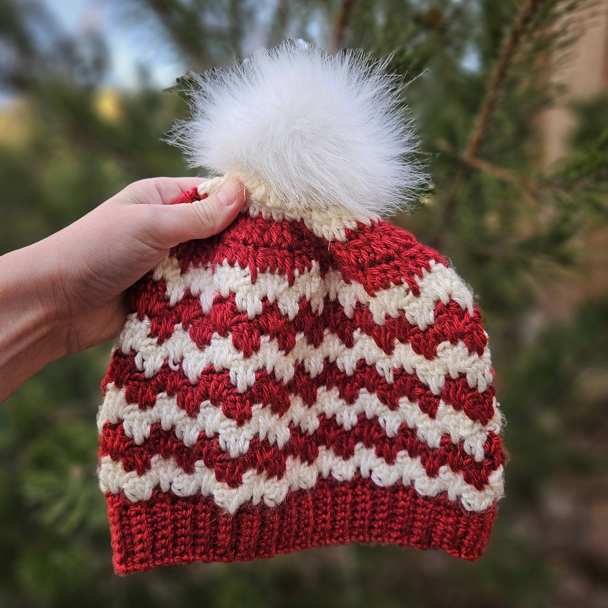 Hand holding a crocheted red and white stripped beanie that has a zig zag pattern from spike stitches