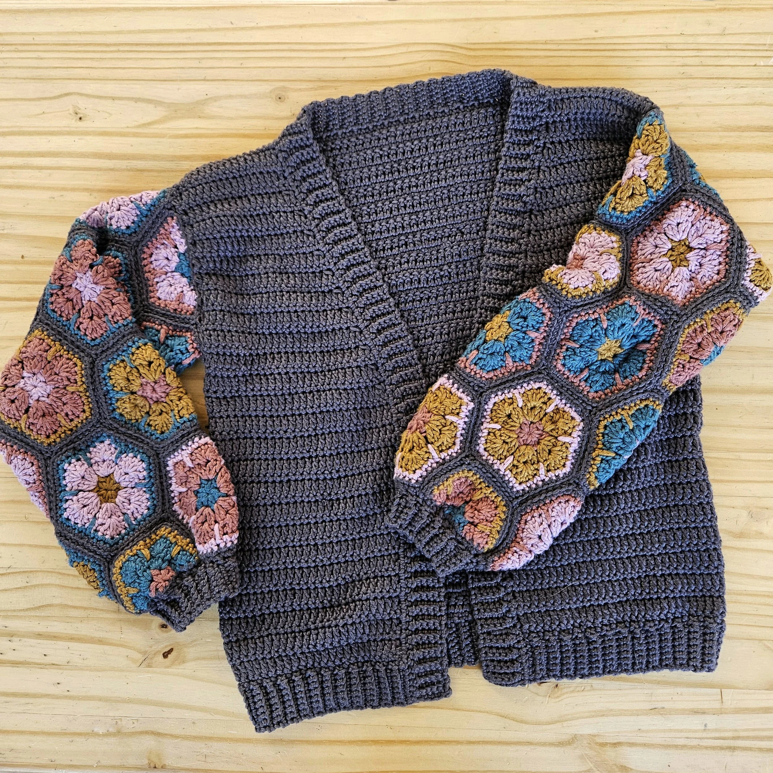 Crochet Flower Power Cardigan laid flat, showcasing vibrant motif sleeves and cozy fit.