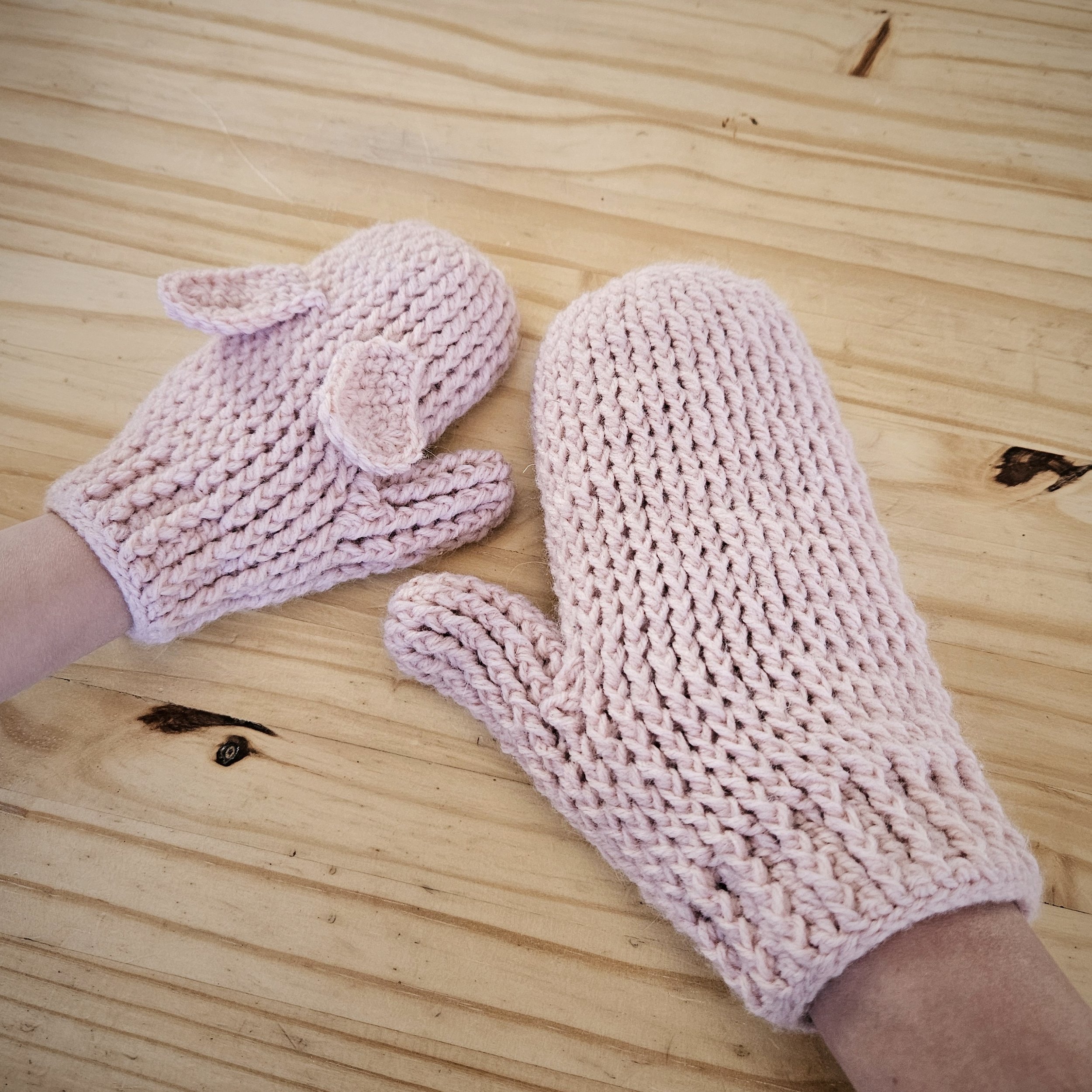 A pair of crochet mittens with adorable bunny ears, neatly arranged on a wooden surface.