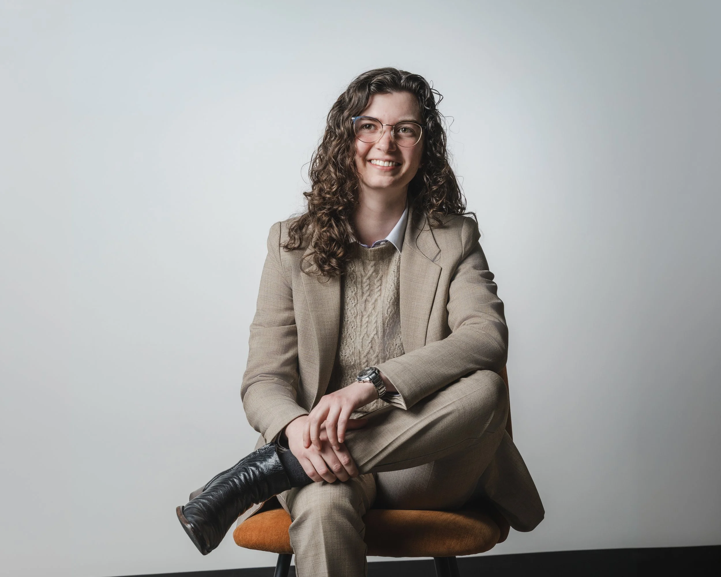 Seated corporate portrait of a woman in a beige suit on a grey background
