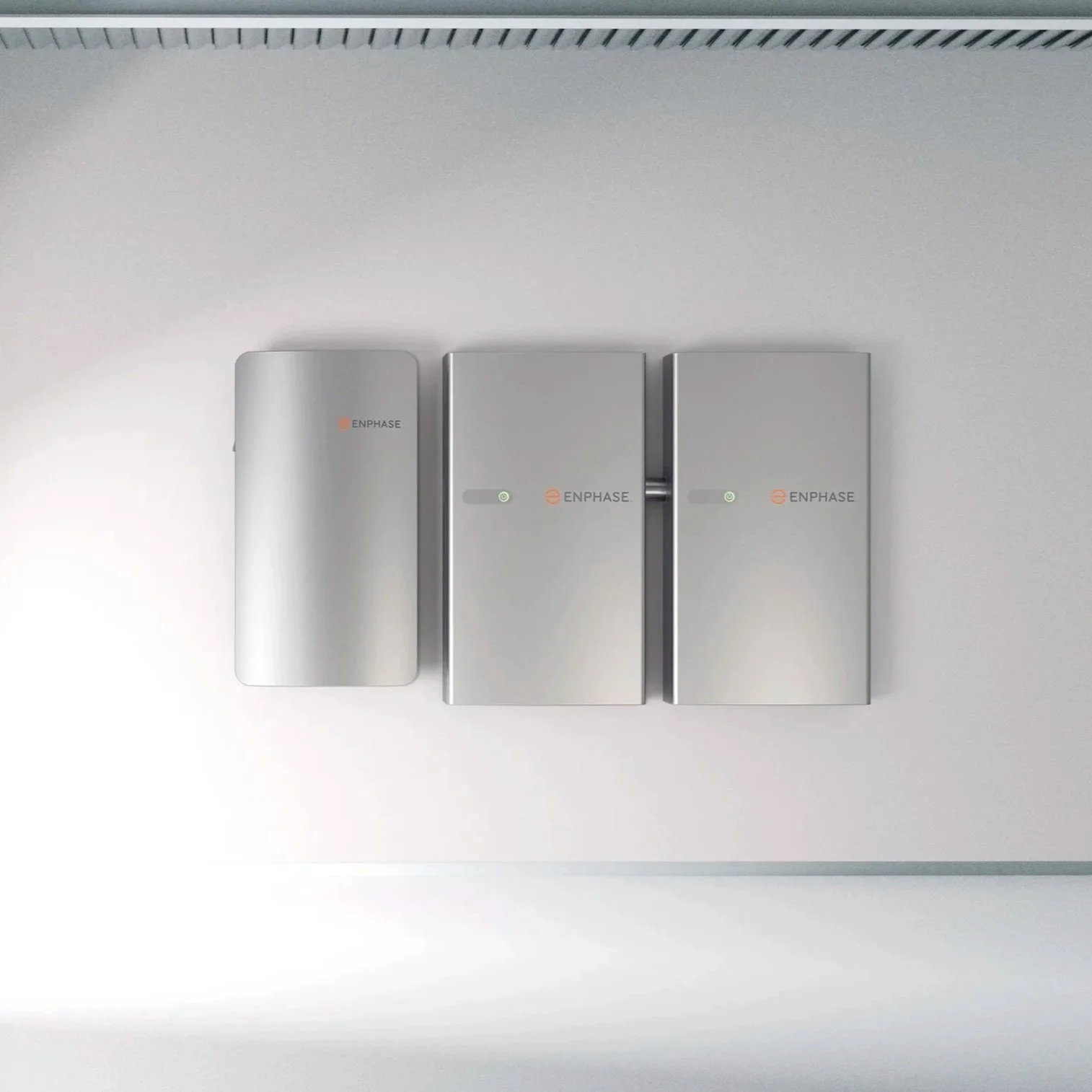 Three silver enphase branded electrical components mounted on a light-colored wall, with the leftmost component smaller and the other two larger and rectangular.