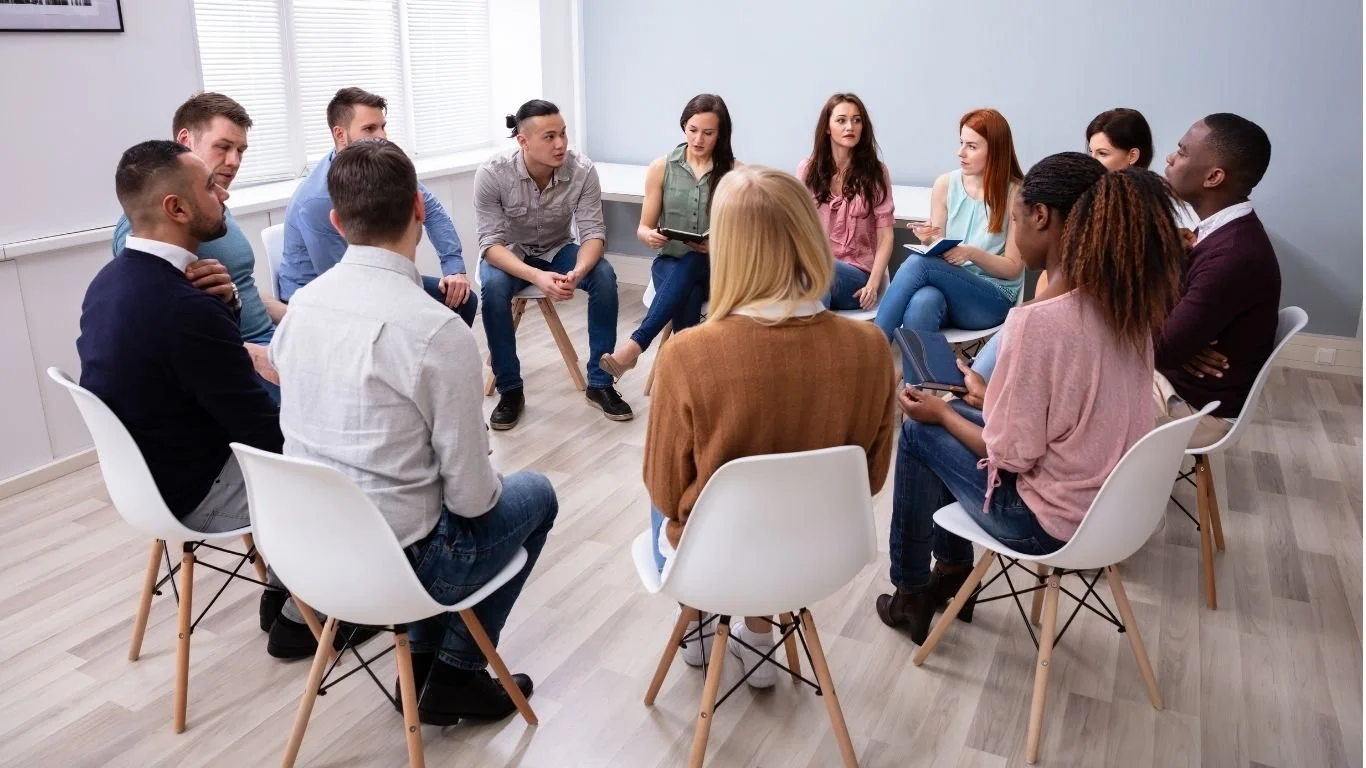 Group of adults seated in a circle engaged in discussion.
