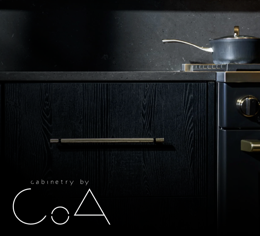 Black kitchen cabinet with a metallic handle, on a dark countertop with a gray cooking pot on a stove.