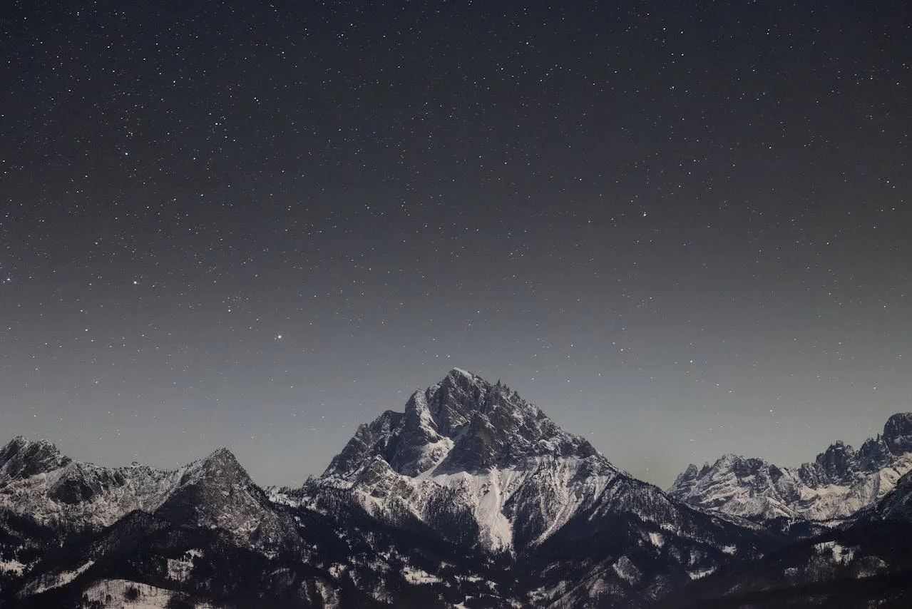 Nightime picture of snow-covered mountain surrounded by stars