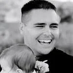 A black and white photo of a man smiling while holding a child.