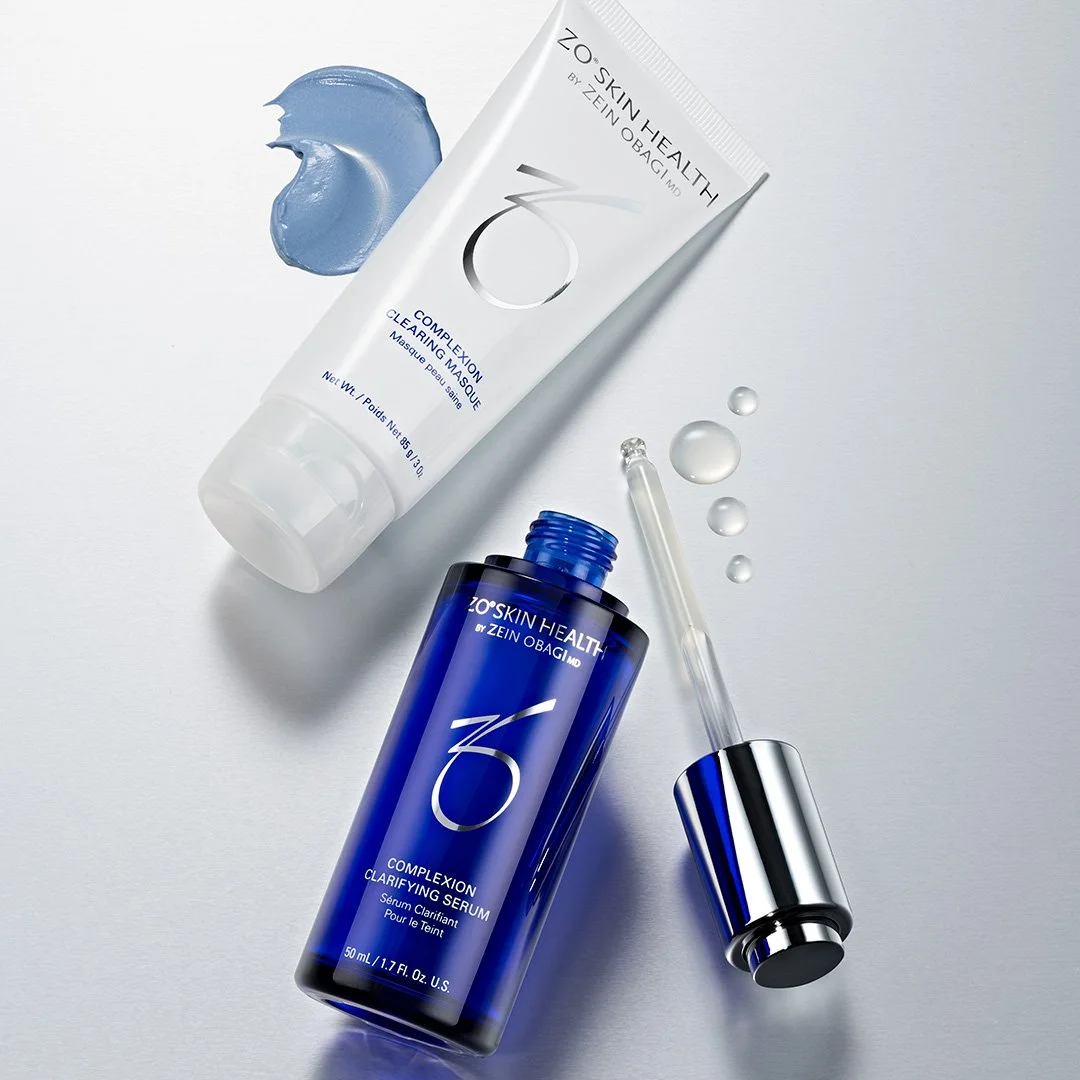 Skincare products from ZO Skin Health by Zein Obagi MD. Includes a white tube of Clearing Mask with a blue cream swatch, a blue bottle of Clarifying Serum with a dropper cap, and a few drops of serum on a white background.