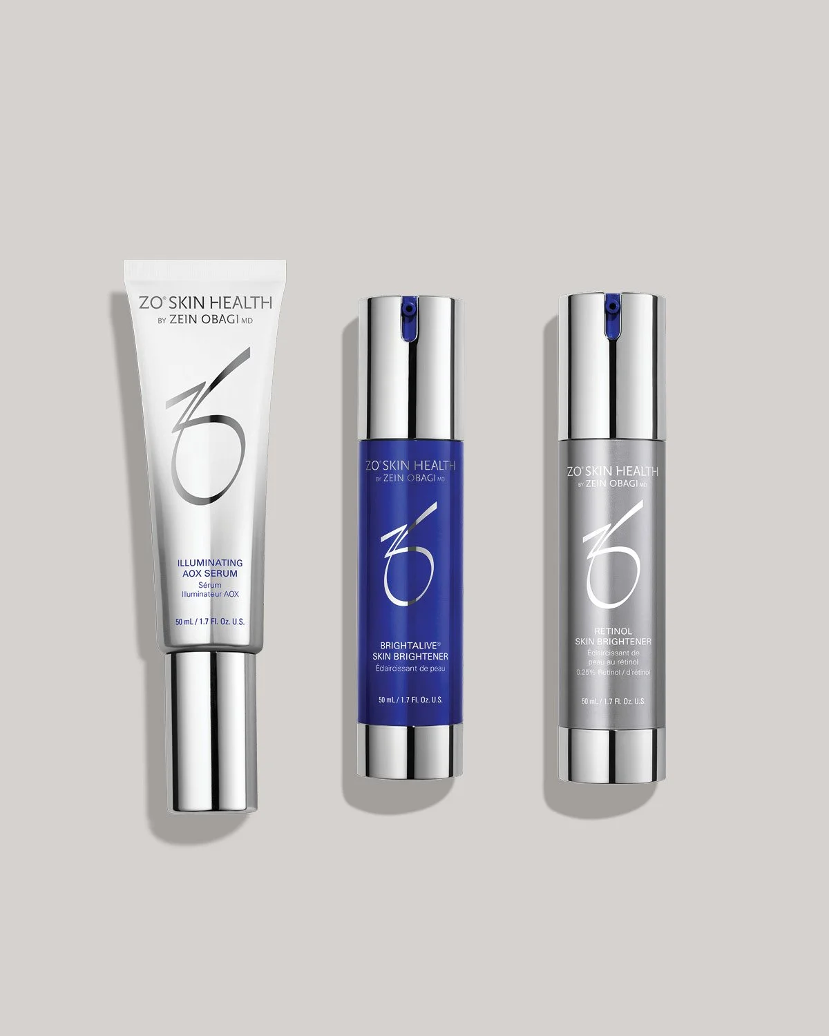 Three bottles of skincare products from ZO Skin Health, including an illuminating AOX serum, a brightening skin brightener, and a retinol skin brightener, all with silver and blue packaging on a light gray background.