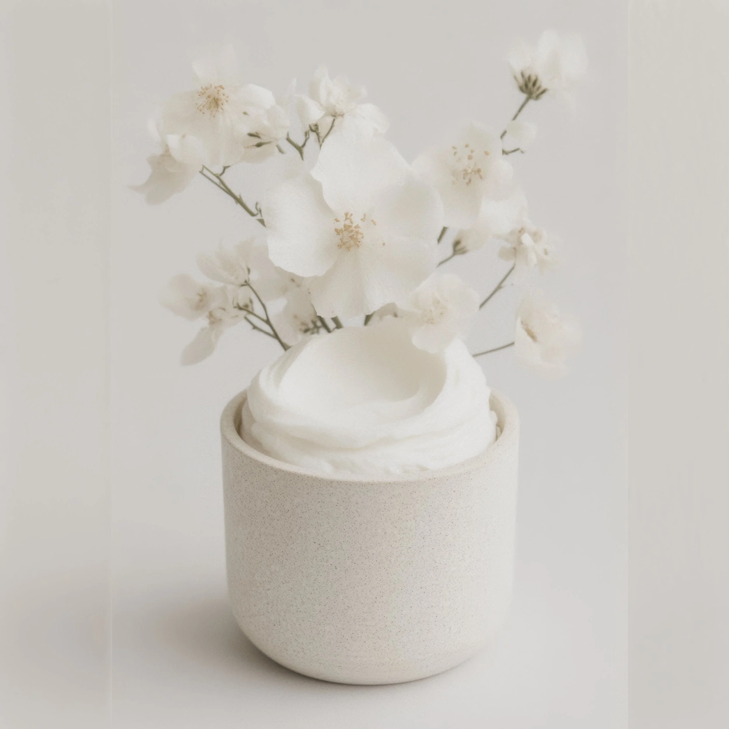 A minimalist beige cup filled with white whipped cream or frosting, decorated with white flowers in the background.