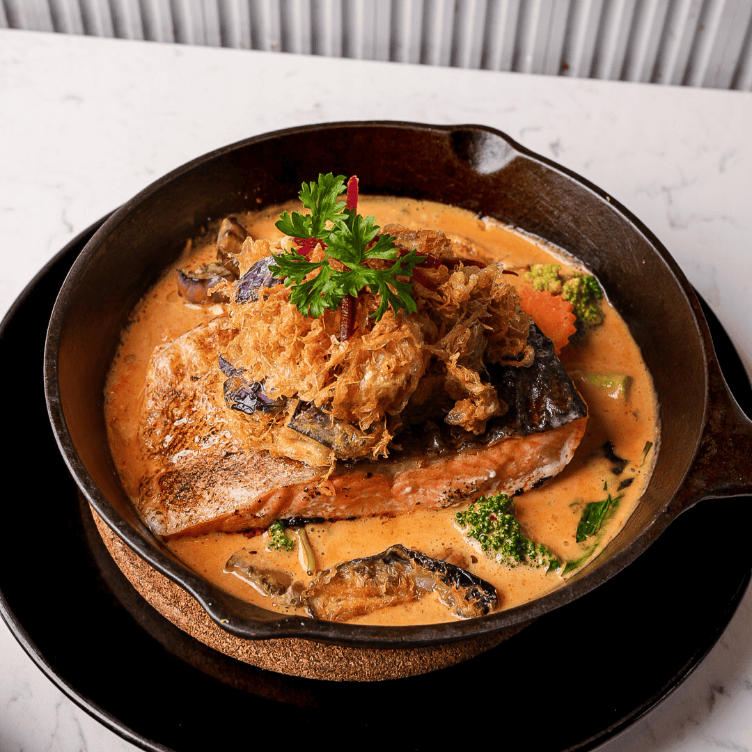 A cooked piece of fish served in a creamy orange sauce with vegetables and topped with fried onions and a sprig of parsley.