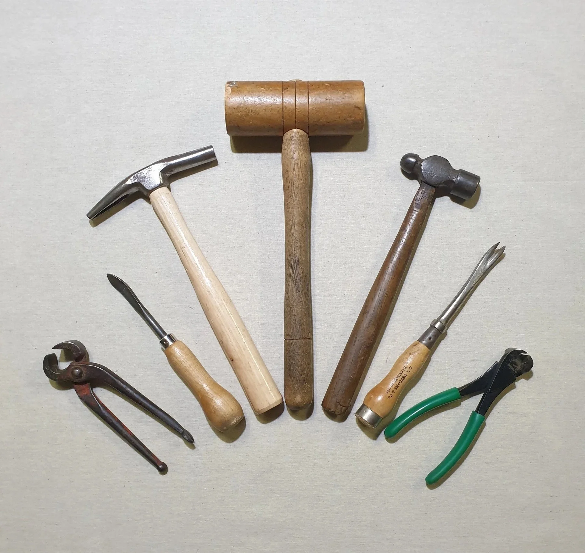 An arrangement of various hand tools, with two hammers in the center, surrounded by pliers, a chisel, and other tools, all laid out on a flat surface.