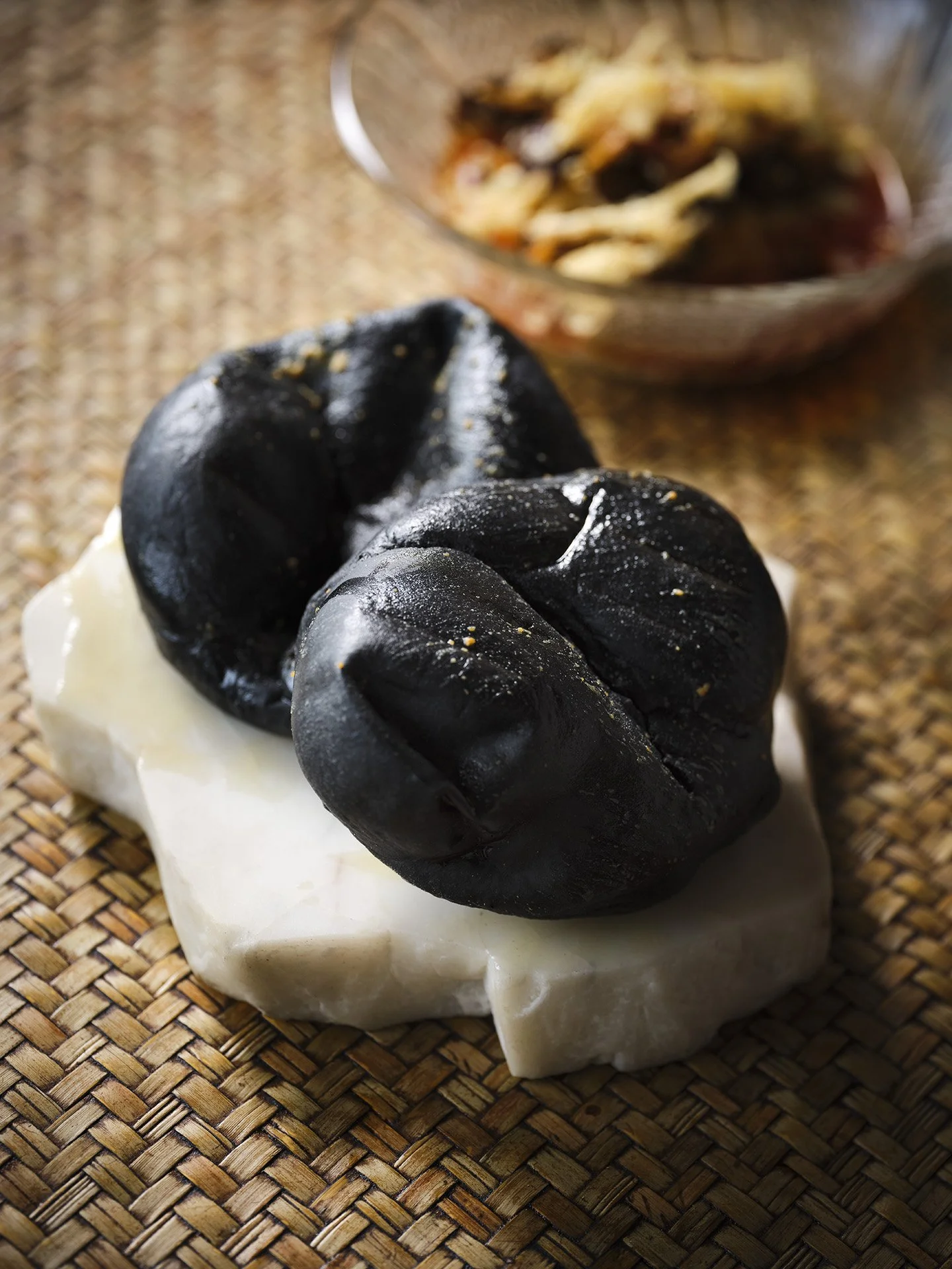 Black truffles on white cheese, with a bowl of sliced cheese in the background.