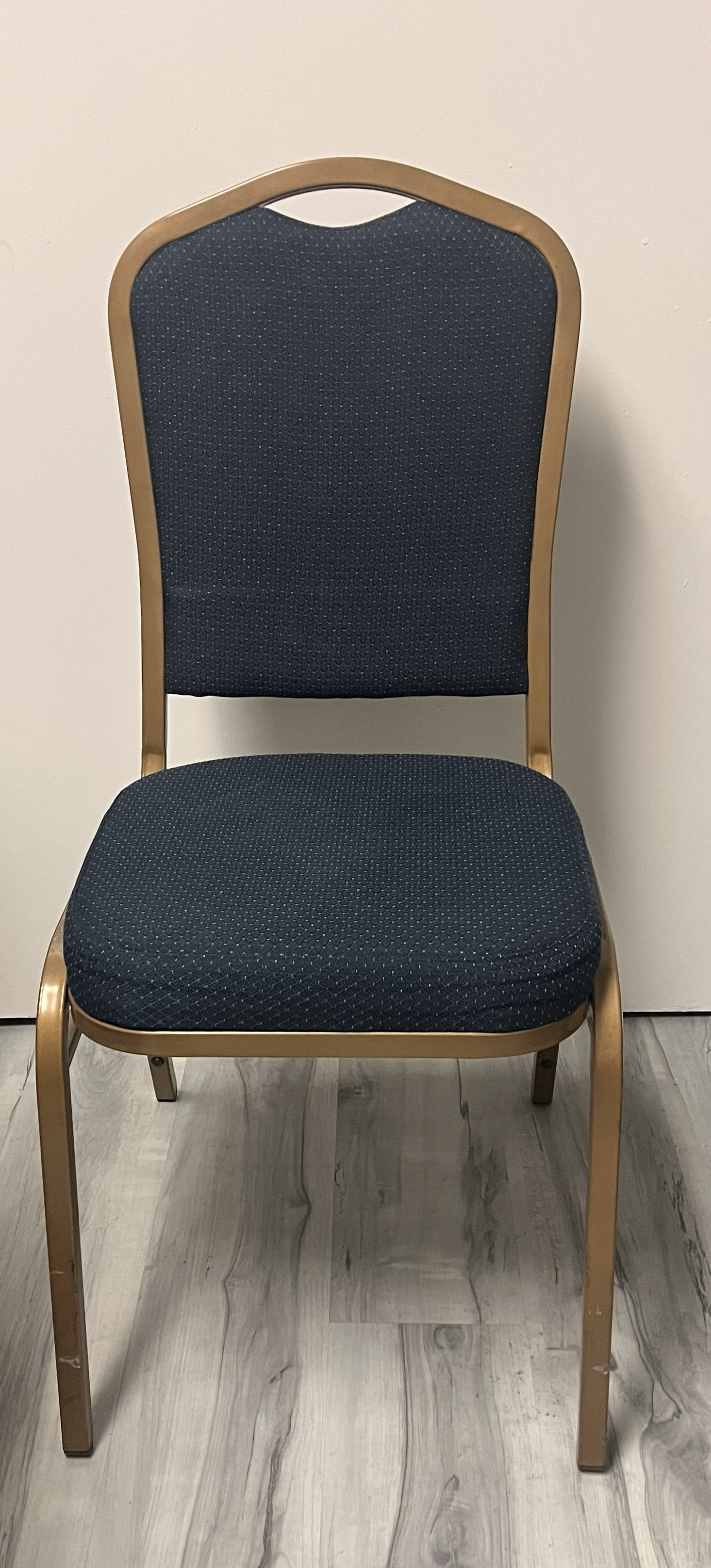 A blue padded chair with a gold-colored metal frame against a white wall.