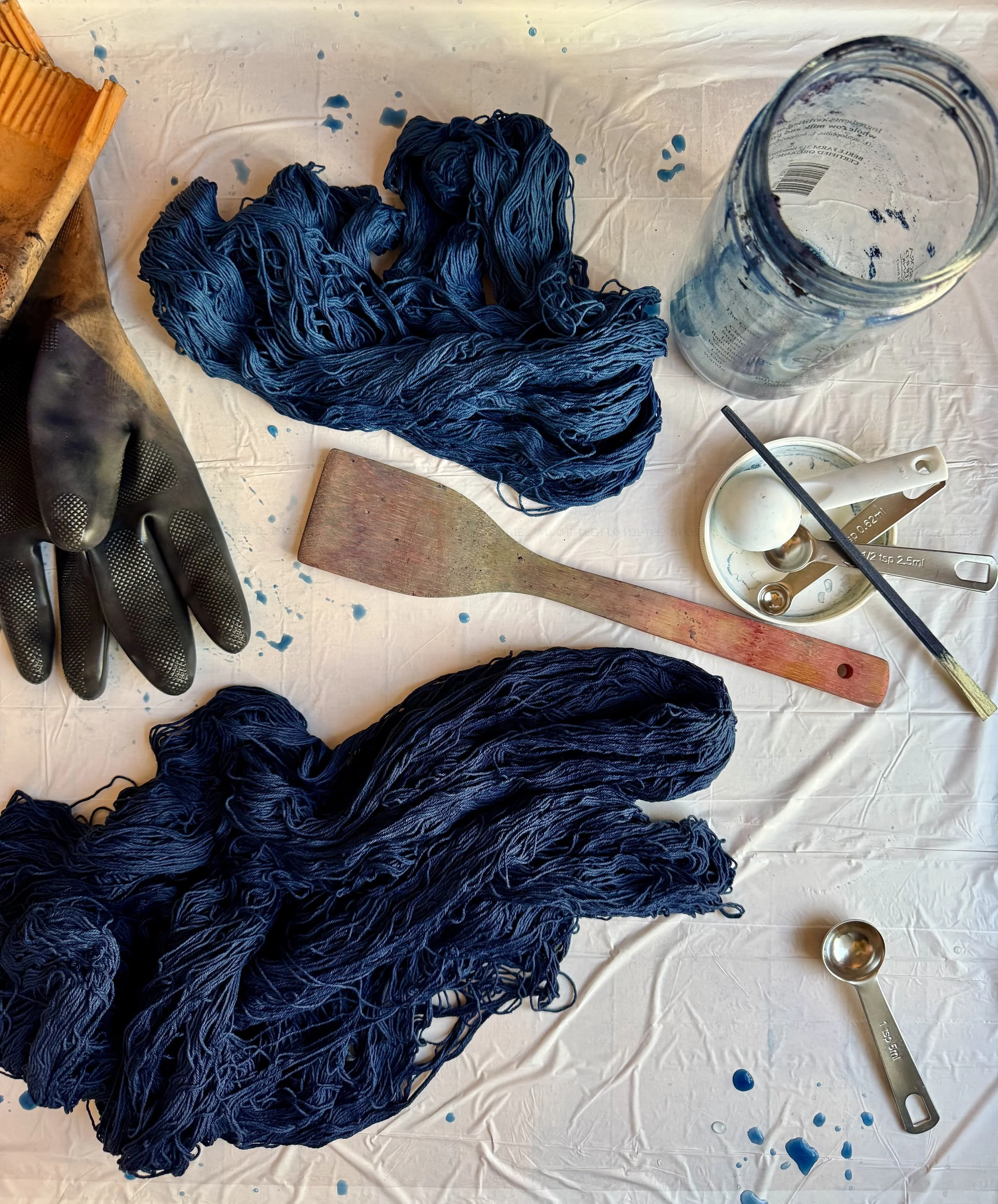 several skeins of indigo-dyed cotton yarns rest on a surface with various natural dye tools