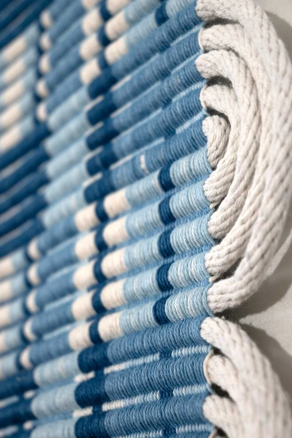 a detailed image of an indigo-dyed rep piece with various shade of indigo dyed yarns creating boxes and stripes in the woven pattern and cotton clothesline weft creating semicircles on the edge of the piece
