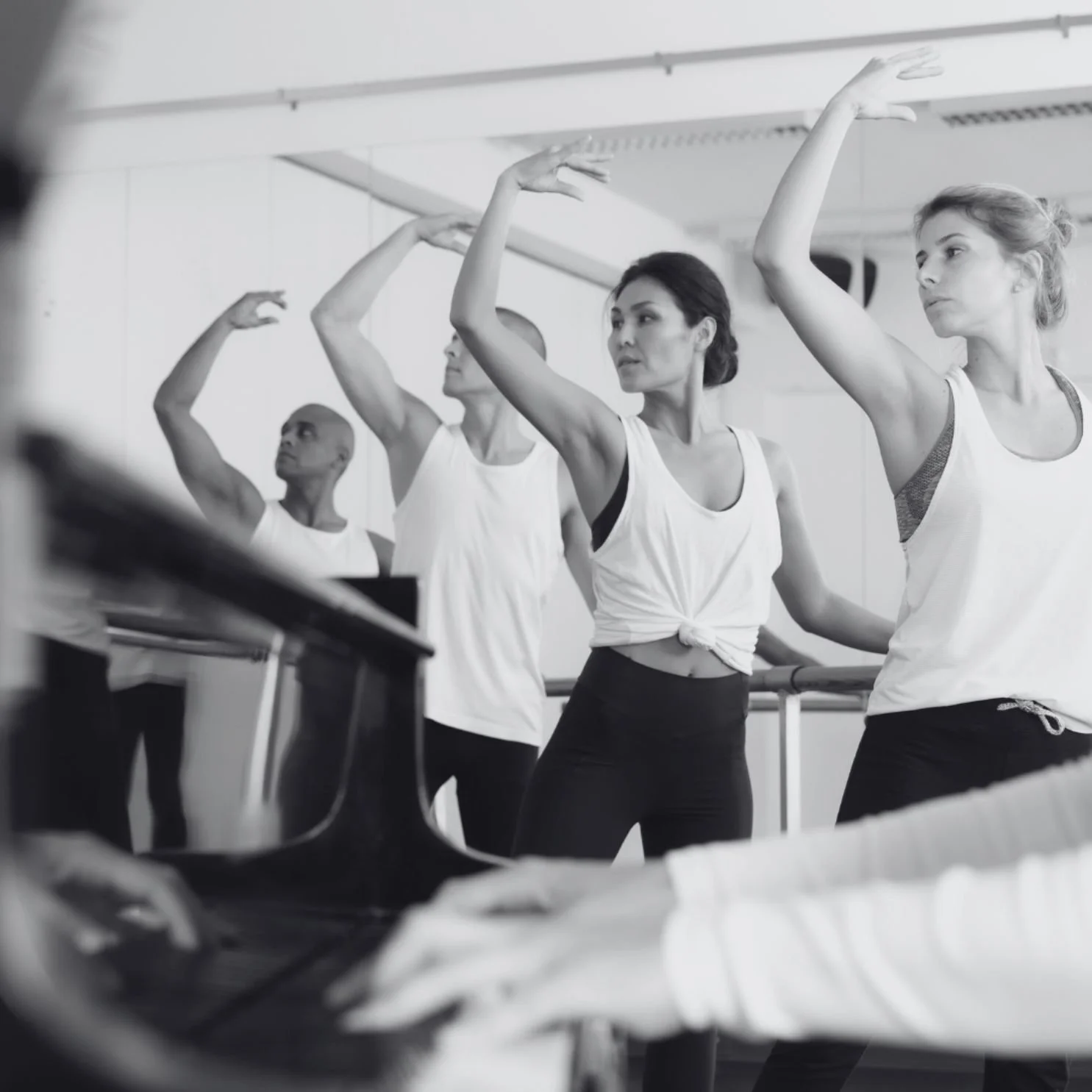 Group of ballet dancers in a studio practicing in front of a mirror with a pianist playing a grand piano.