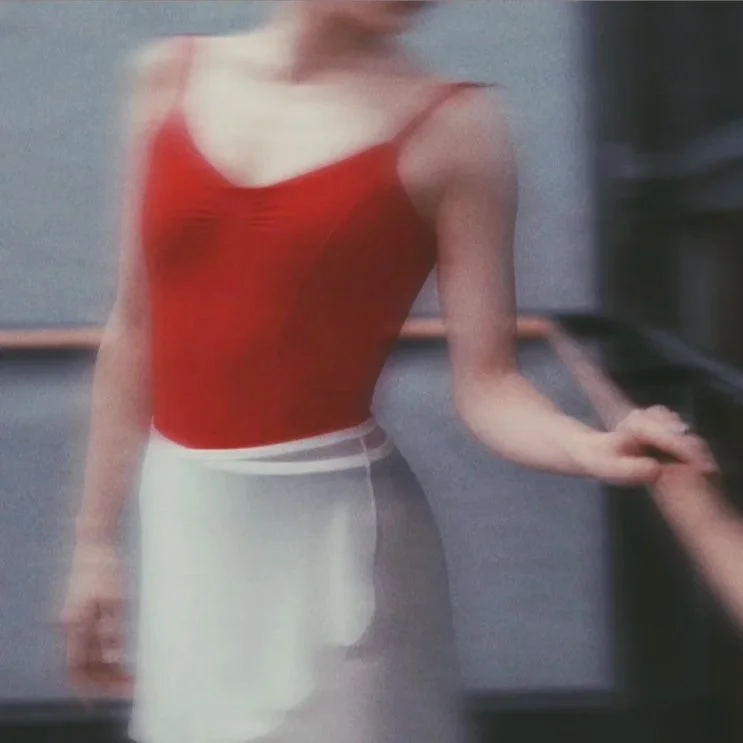 A person wearing a red sleeveless top and a white skirt, standing in front of a gray background.