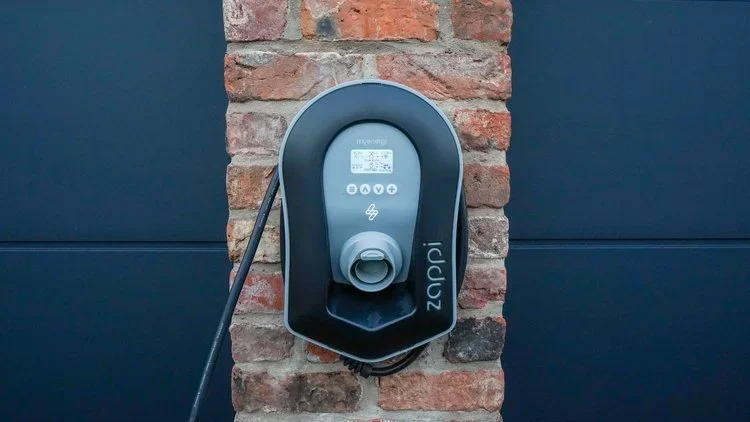 Electric vehicle charging station mounted on a brick wall between two dark panels.