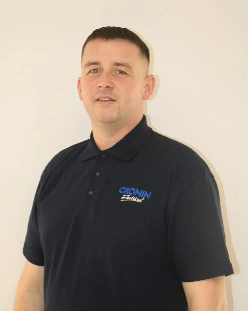 Man wearing black polo shirt with 'CROVIN Electrical' logo, standing against a plain white wall.