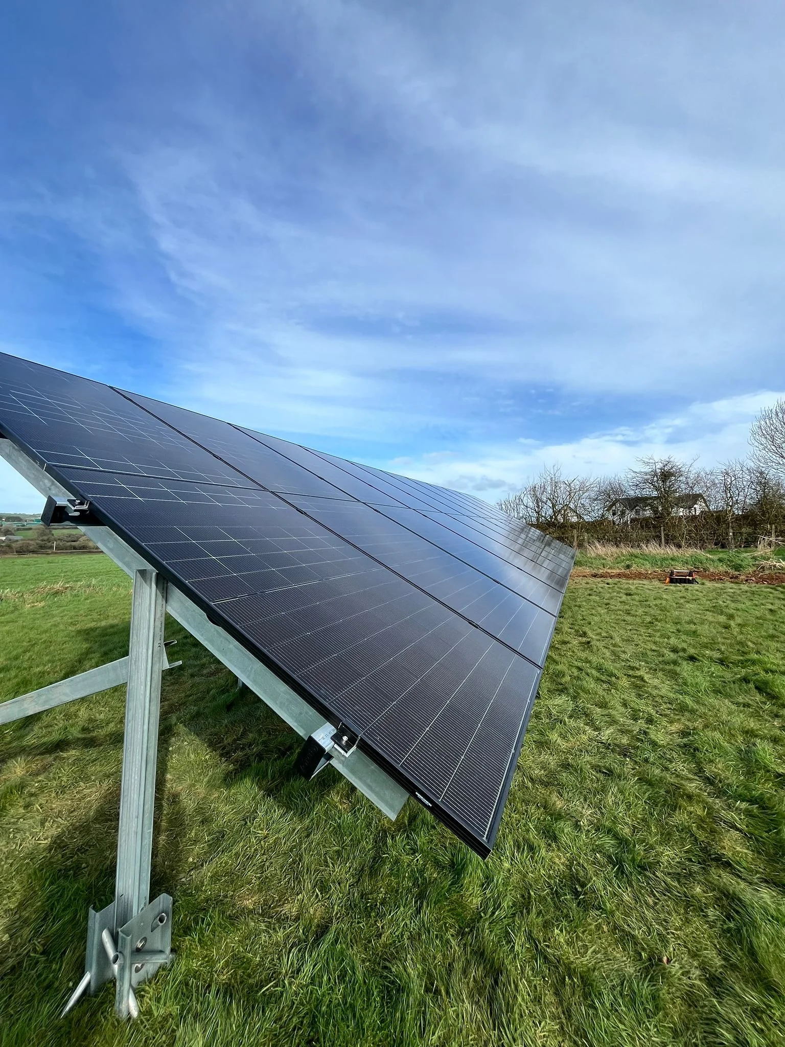 Solar panel array installed on a grassy field with a partly cloudy sky overhead.