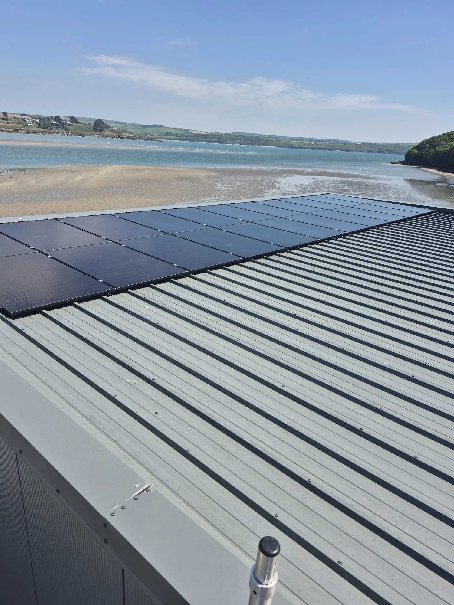 Solar panels installed on a metal rooftop overlooking a beach and body of water.