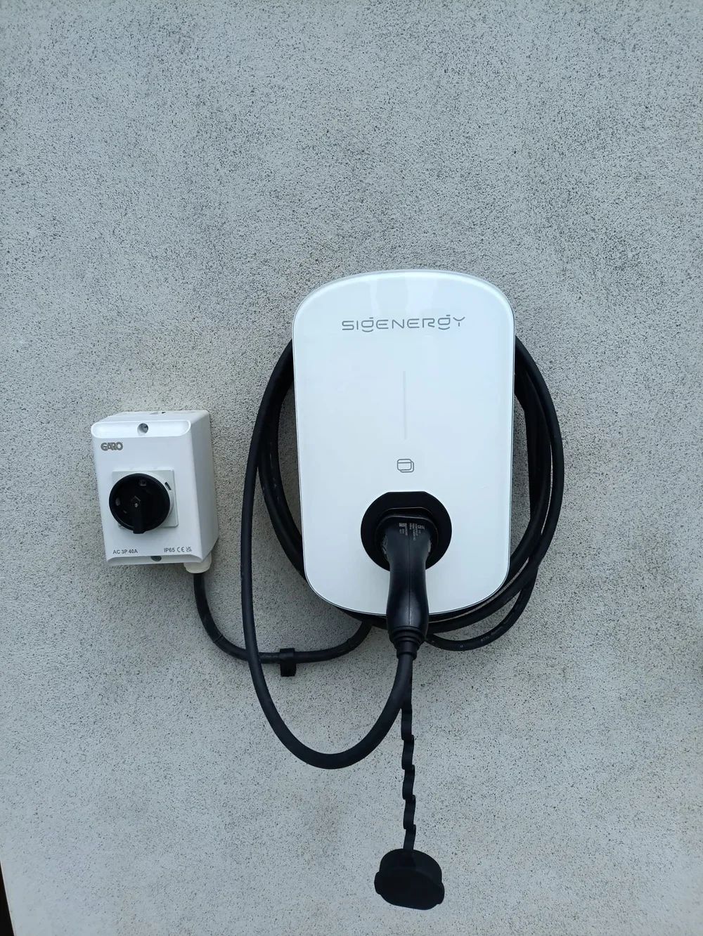 Electric vehicle charging station with a cable plugged into an outlet on a textured wall.