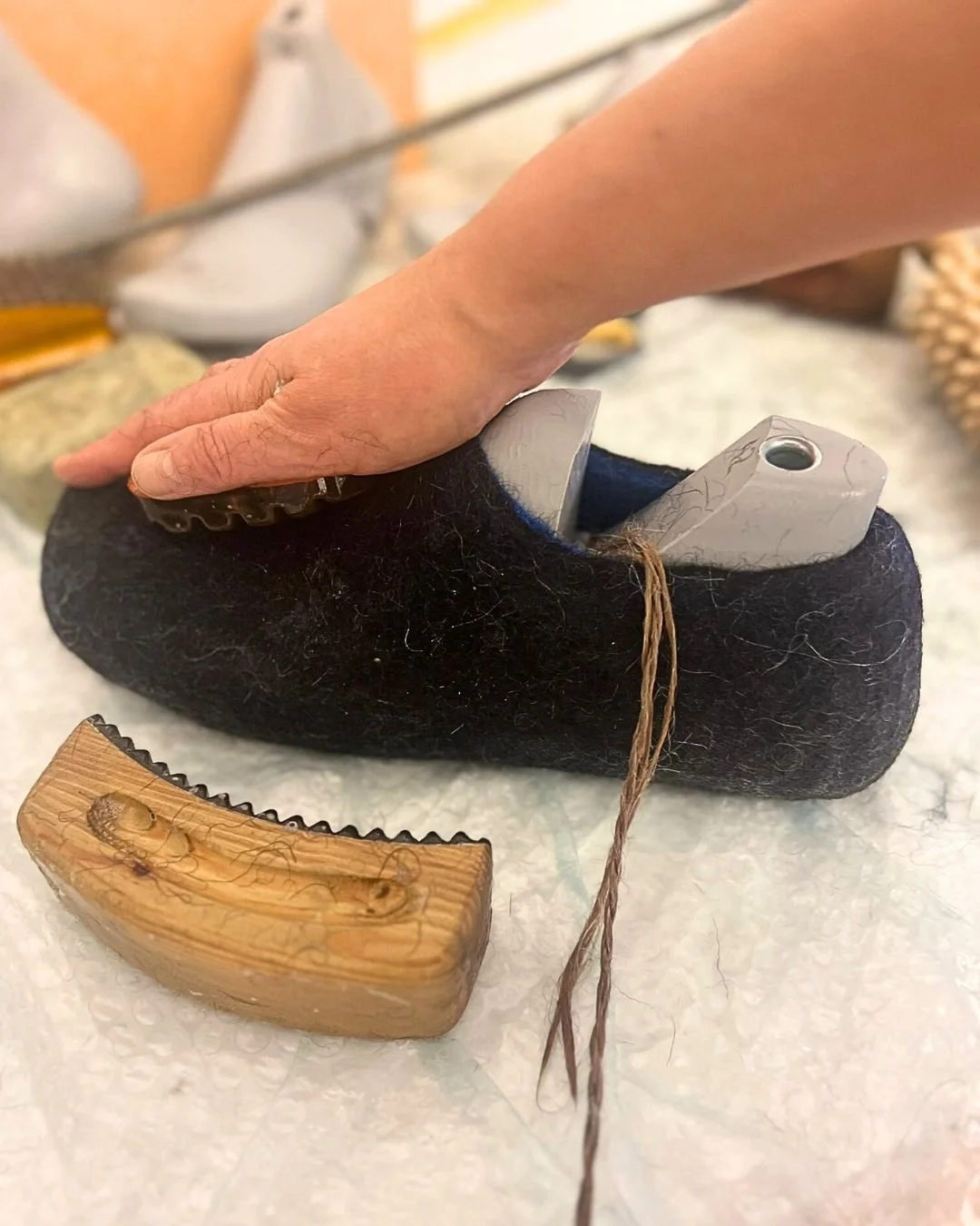 Dovile Sirmulyte hand-sculpting a dark charcoal wool slipper on a wooden last in her Feltforma studio in Vilnius, Lithuania — each pair made by hand from mulesing-free Tyrolean mountain wool, glue-free and plastic-free