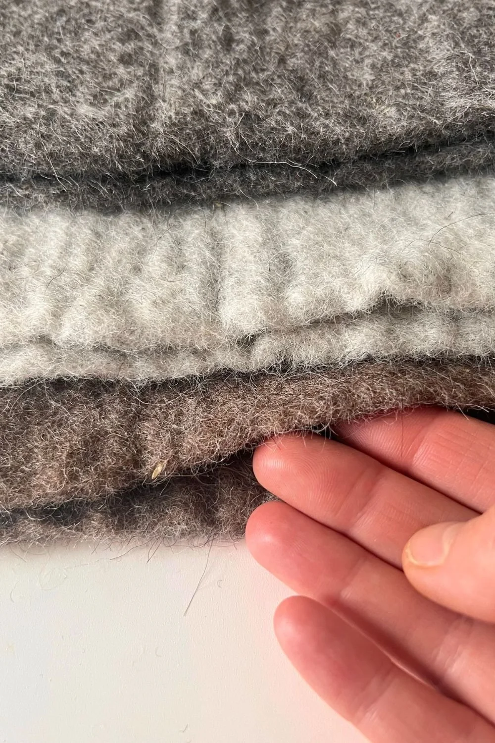 Close-up of dense undyed wool in natural shades, soft and thick, the wool Dovilė sculpts into sauna hats.