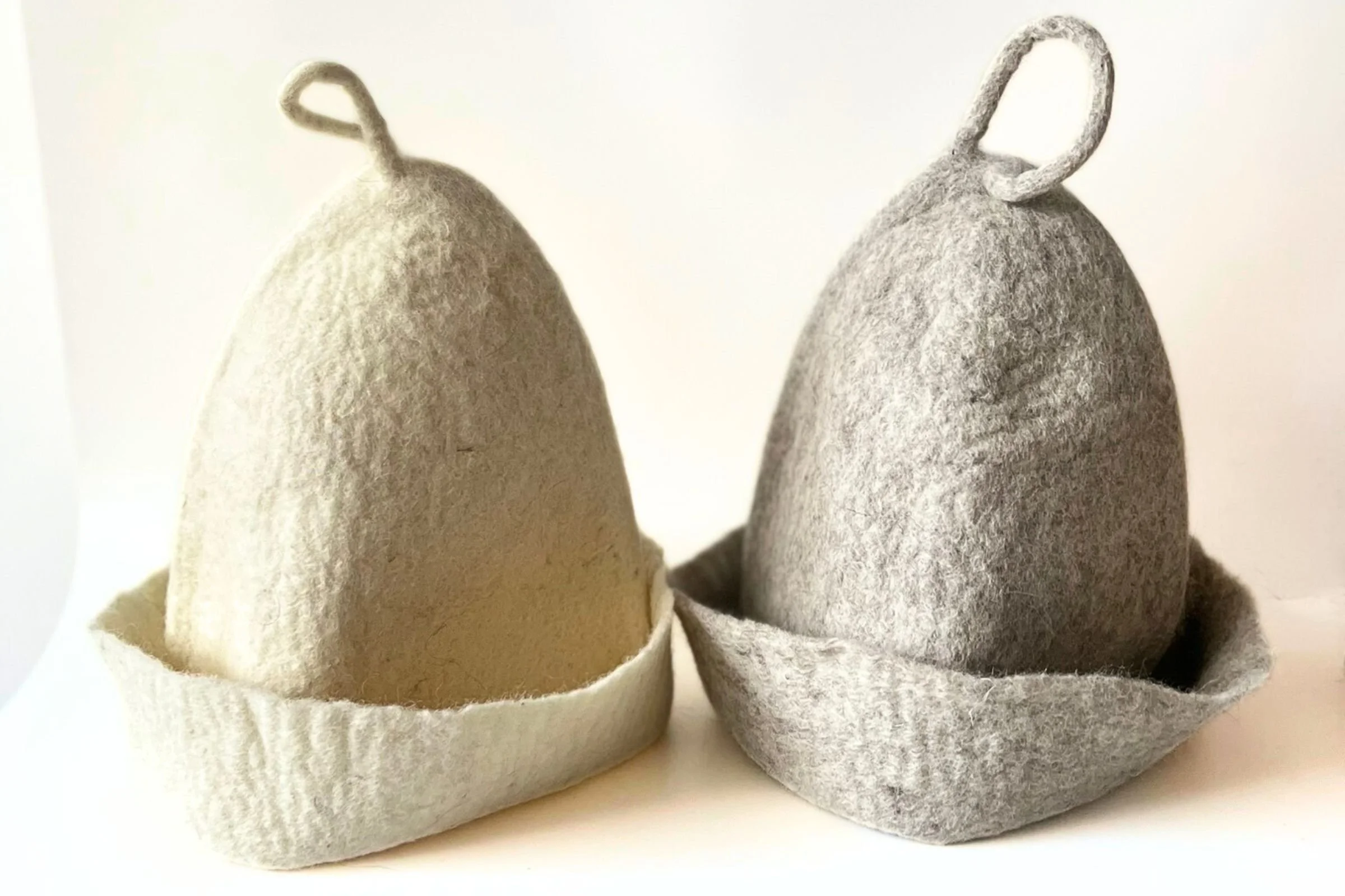 Undyed wool sauna hats hand sculpted from natural felt, shown with folded brim and hanging loop for adjustable fit and traditional sauna use