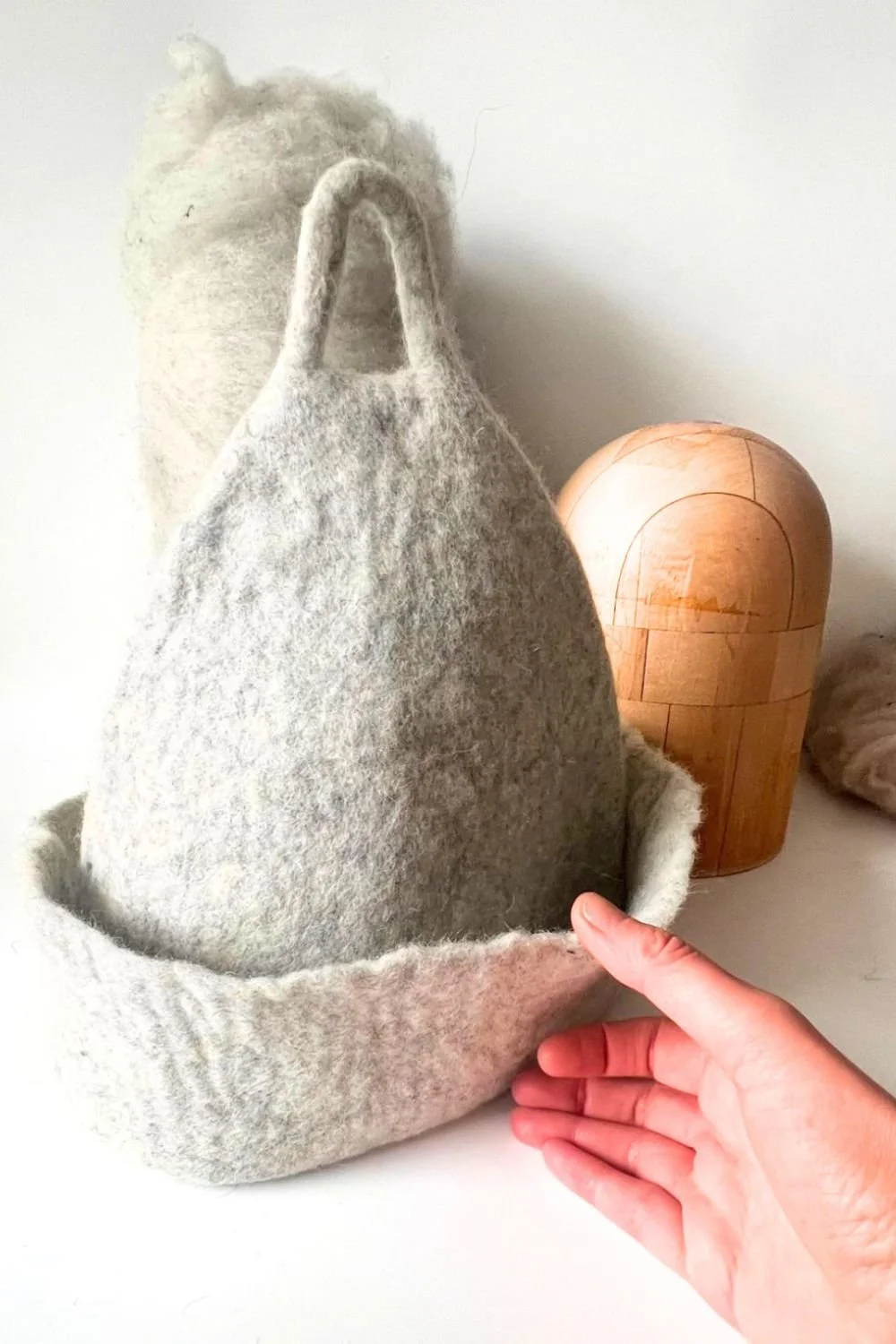 Hand-sculpted undyed wool sauna hat in natural cream, standing in its finished shape.