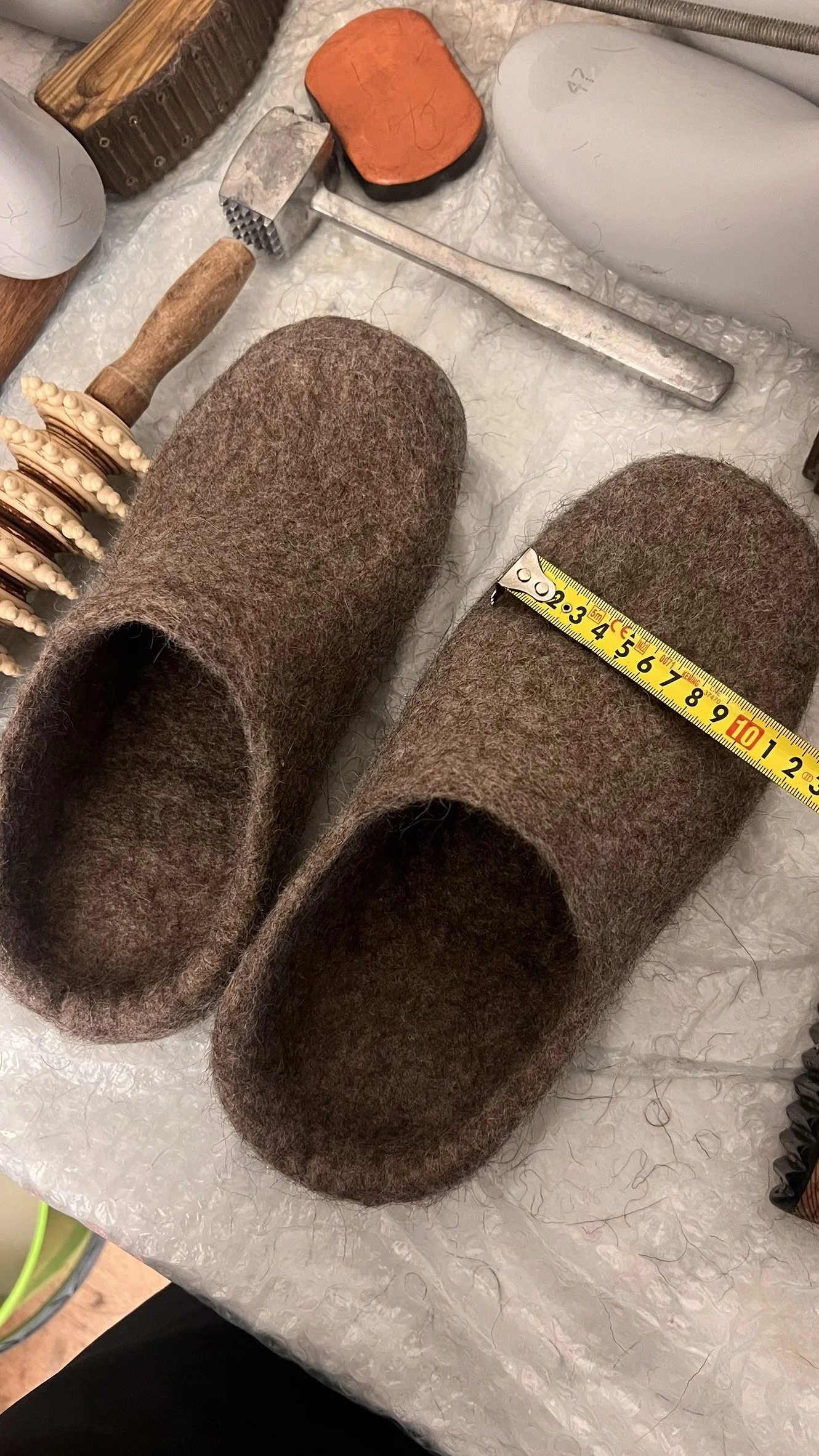 Feltforma handmade undyed wool slippers in Chestnut Cocoa being measured with a tape measure — custom sizing for wide feet, bunions, and high instep. Every pair hand-sculpted to your exact foot measurements