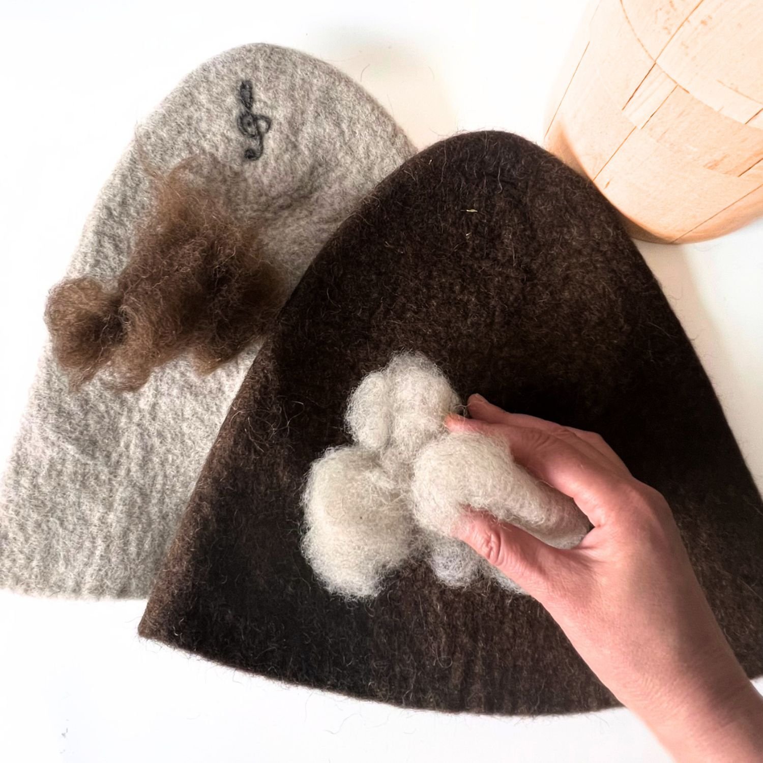 Light undyed wool placed on a brown wool sauna hat to choose a contrasting color for a visible custom design