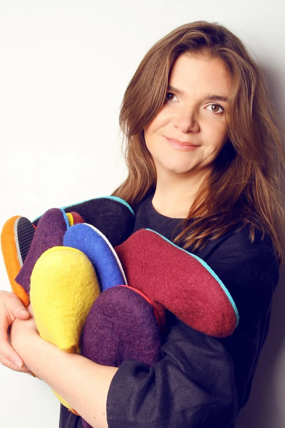 Dovile Sirmulyte, founder of Feltforma, holding hand-felted wool slippers in Vilnius, Lithuania — maker of undyed wool sauna hats and custom wool slippers for cold plunge recovery and sauna rituals, shipped to the US duty-free