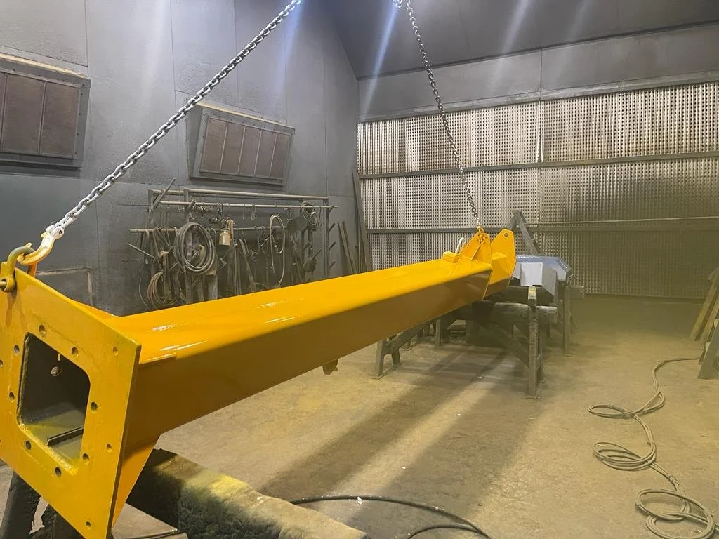 A yellow industrial crane arm hangs from a chain in a workshop with tools and equipment on the wall.