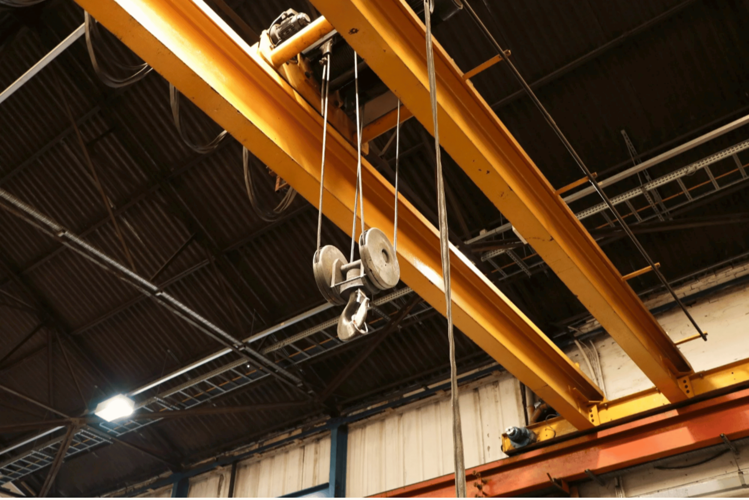 Industrial warehouse ceiling with a large yellow overhead crane and hooks hanging from it.