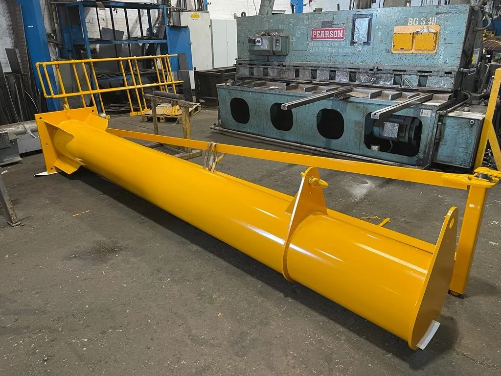 Yellow snow plow blade with attachment hardware in a workshop.