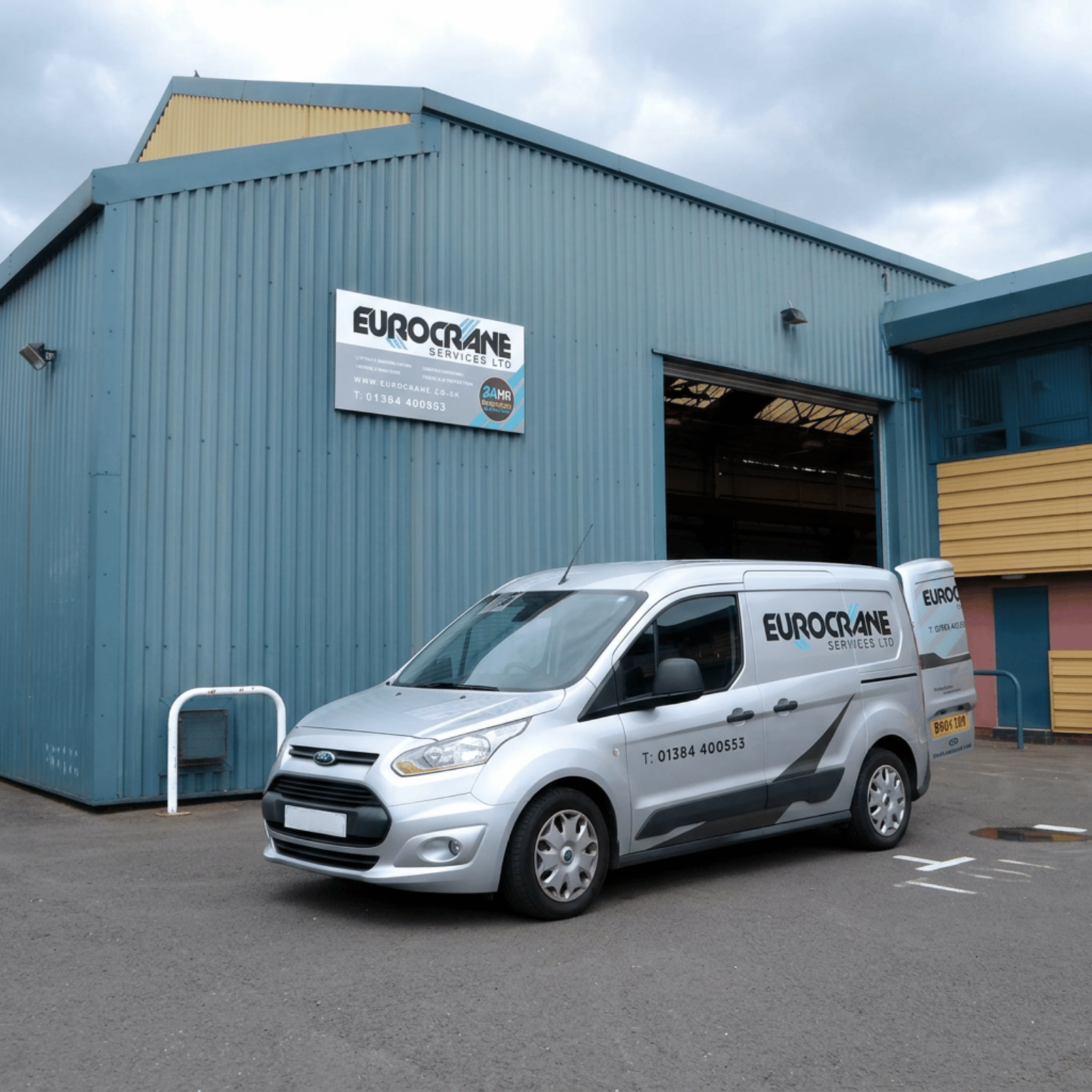 A white delivery van with 'EUROCRANE Services Ltd' branding parked in front of a blue industrial warehouse with a partially open large door.
