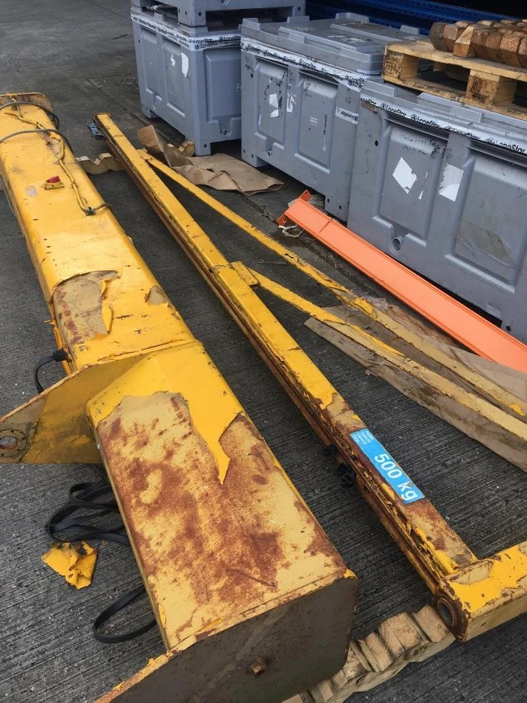 Rusty yellow metal construction or industrial equipment parts placed on the ground in a warehouse or storage area.