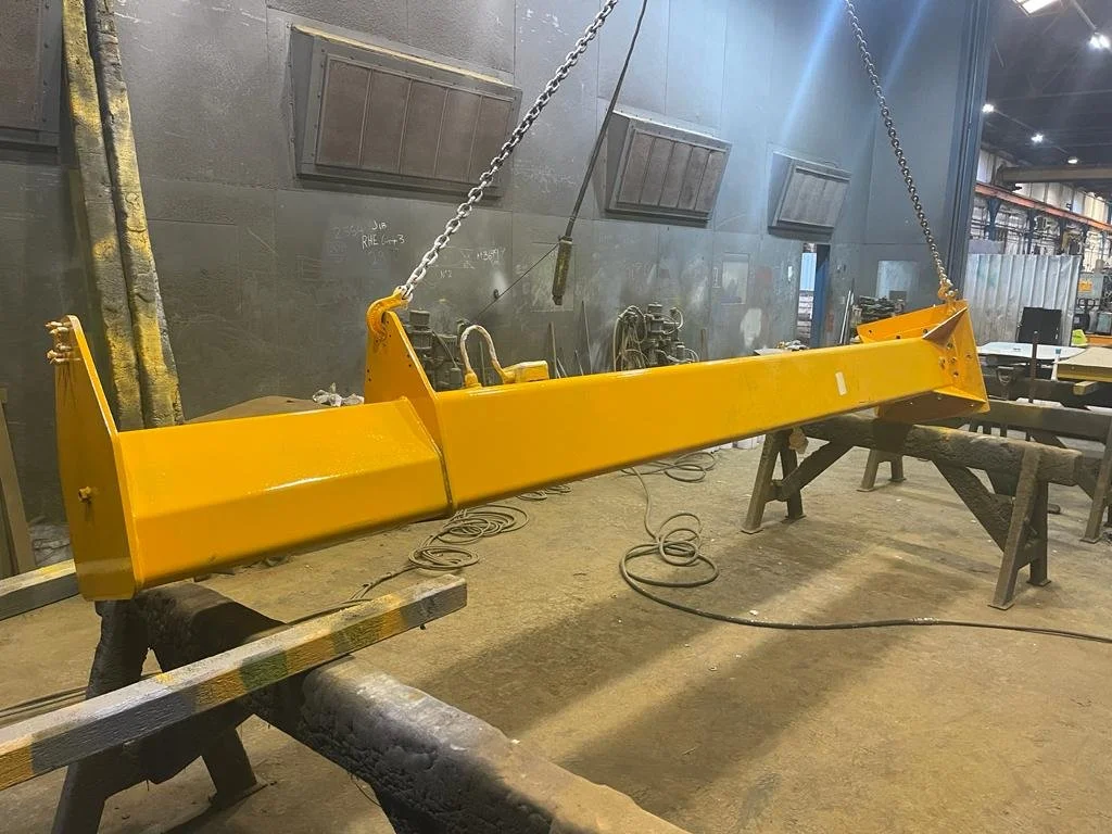 A large yellow metal beam hanging from chains in a manufacturing or industrial workshop.