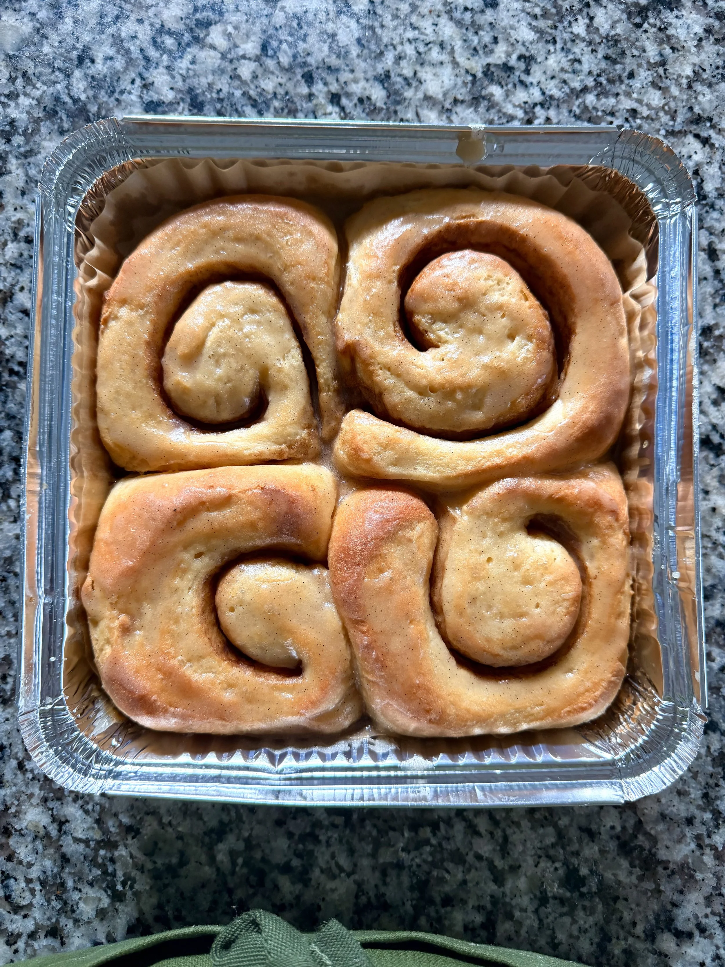 A tray of freshly baked cinnamon rolls in a foil container placed on a granite countertop.
