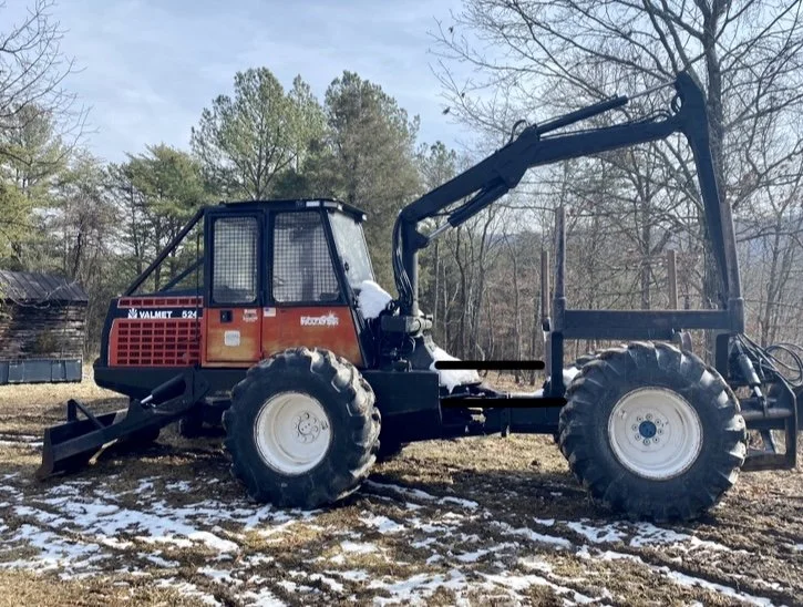 A large black and orange front-end loader tractor parked on a patchy snow-covered ground with trees in the background.