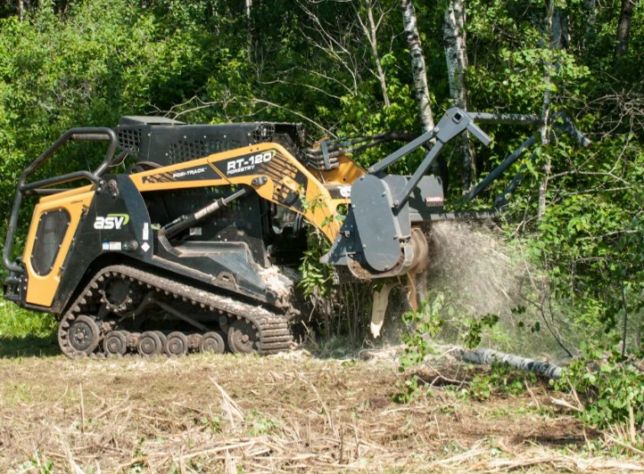 A tracked forestry mulcher clearing trees in a forested area.