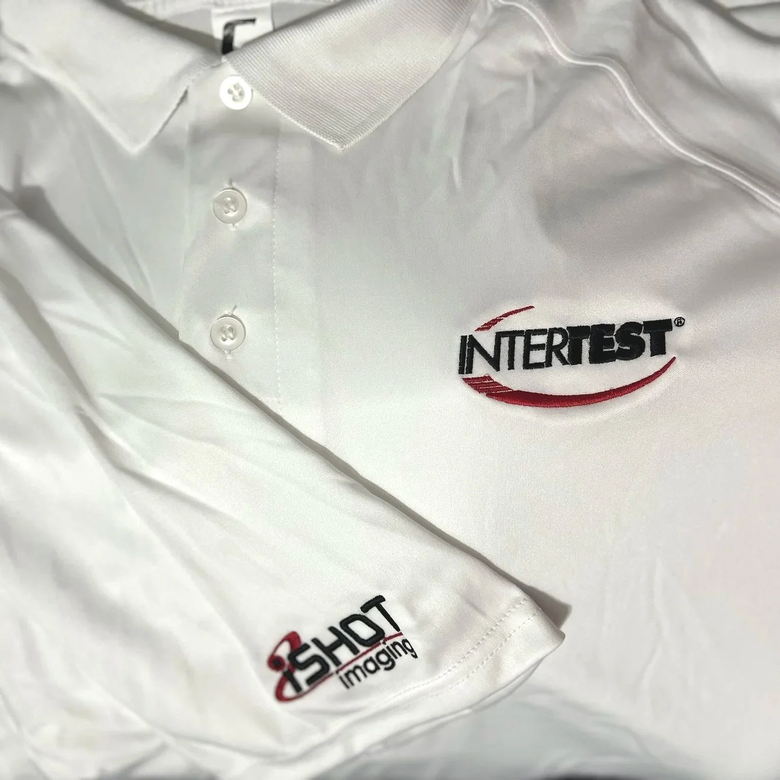 white polo shirt with Intertest logo embroidered on left chest and Ishot logo embroidered on right sleeve