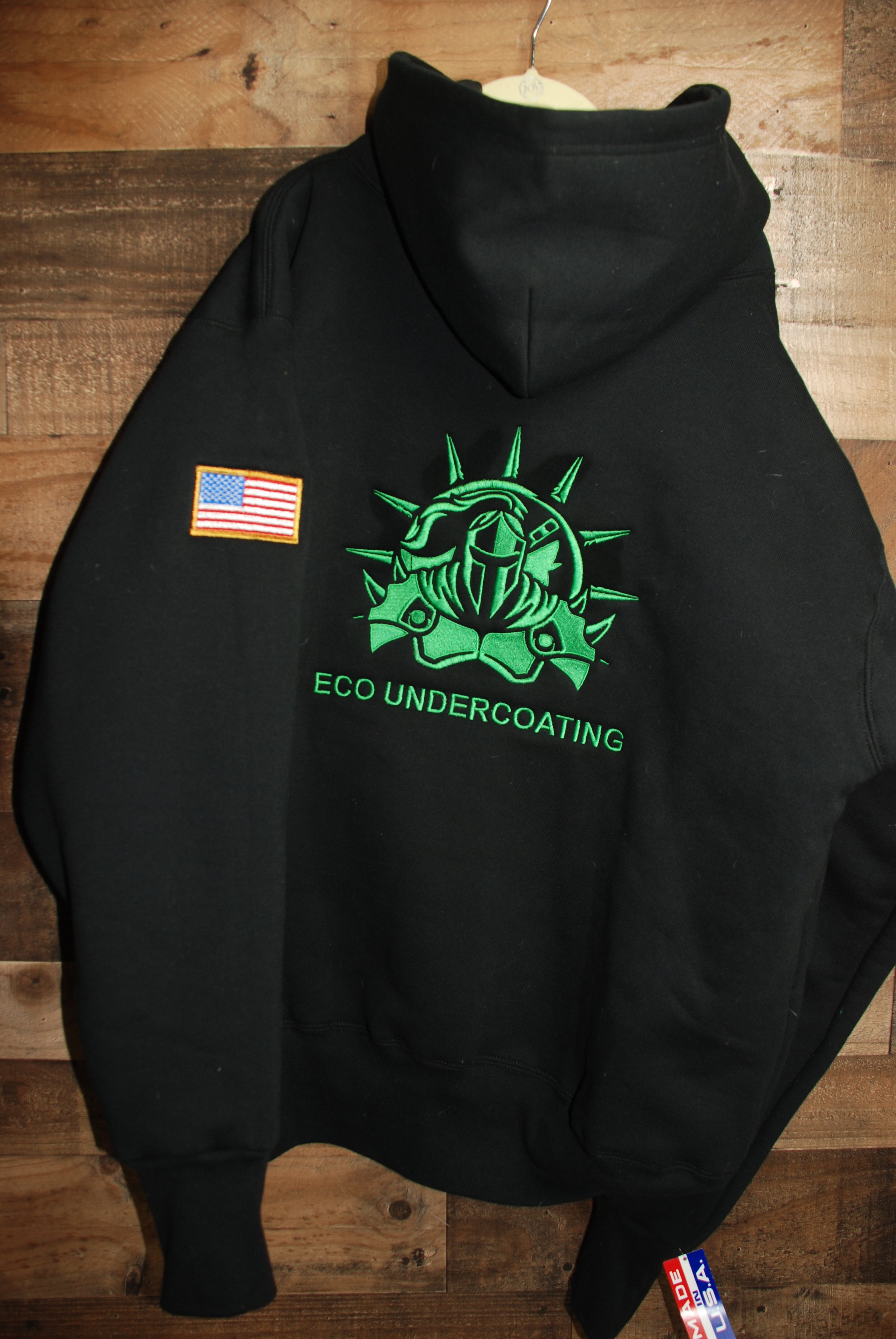 black hooded sweatshirt with green ECO Undercoating logo embroidered on the back and an American flag embroidered on the sleeve