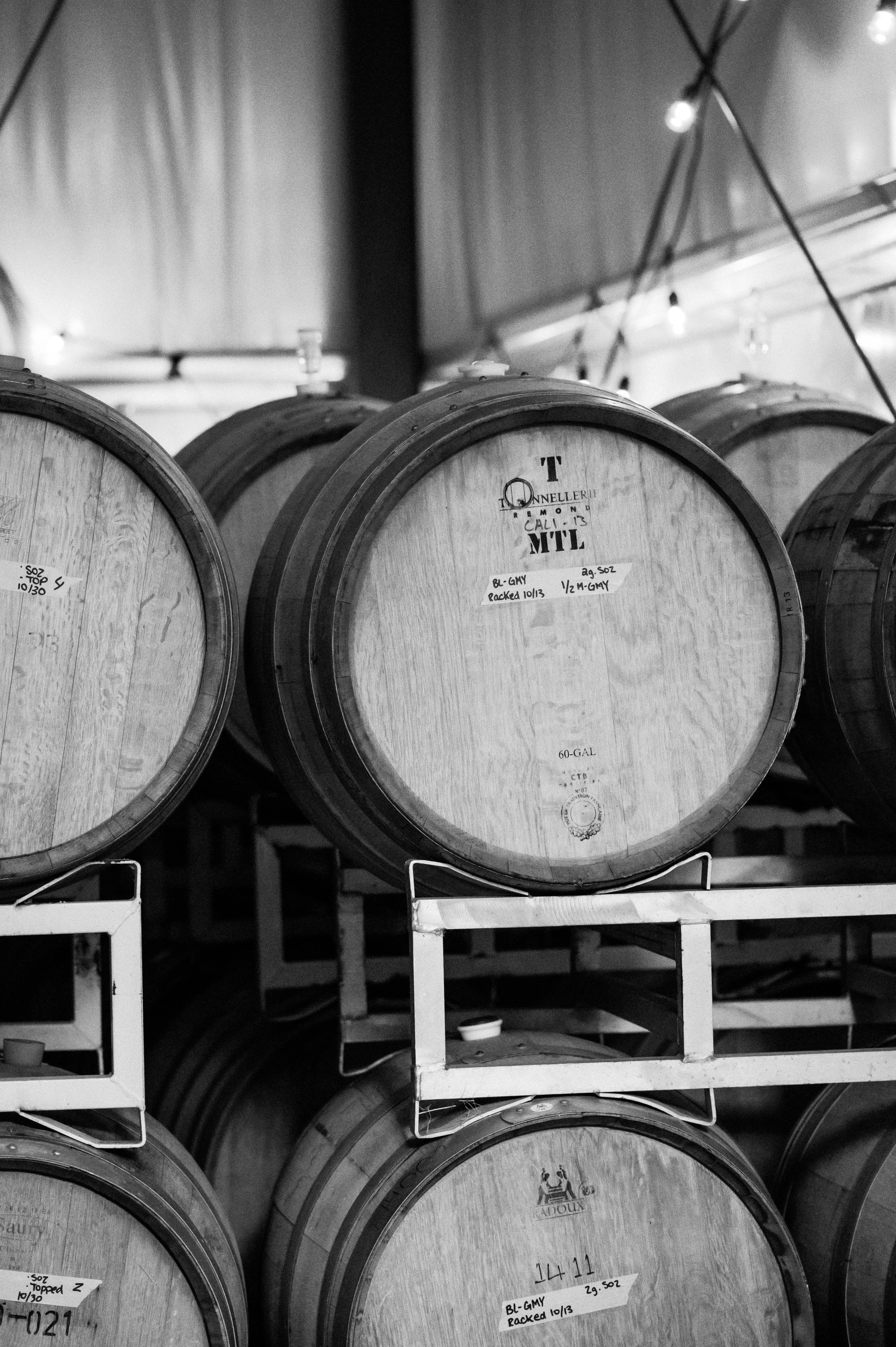 A black and white photo of stacked wine barrels in a winery storage room.