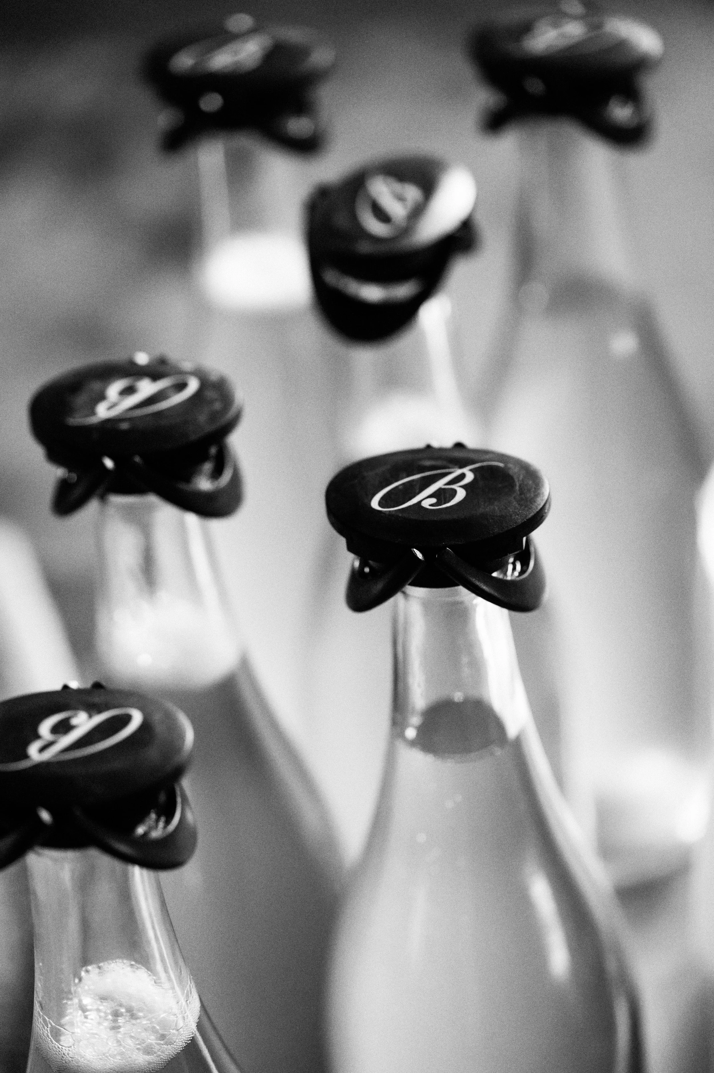 Close-up of sparkling wine bottles with caps marked 'B' in black and white.