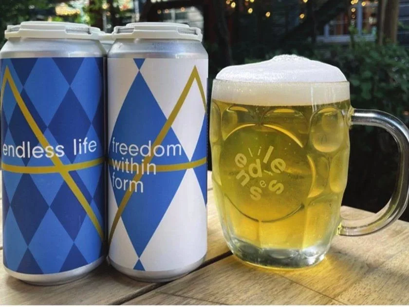Endless Life Brewing pilsner cans beside a full glass of pale golden pilsner
