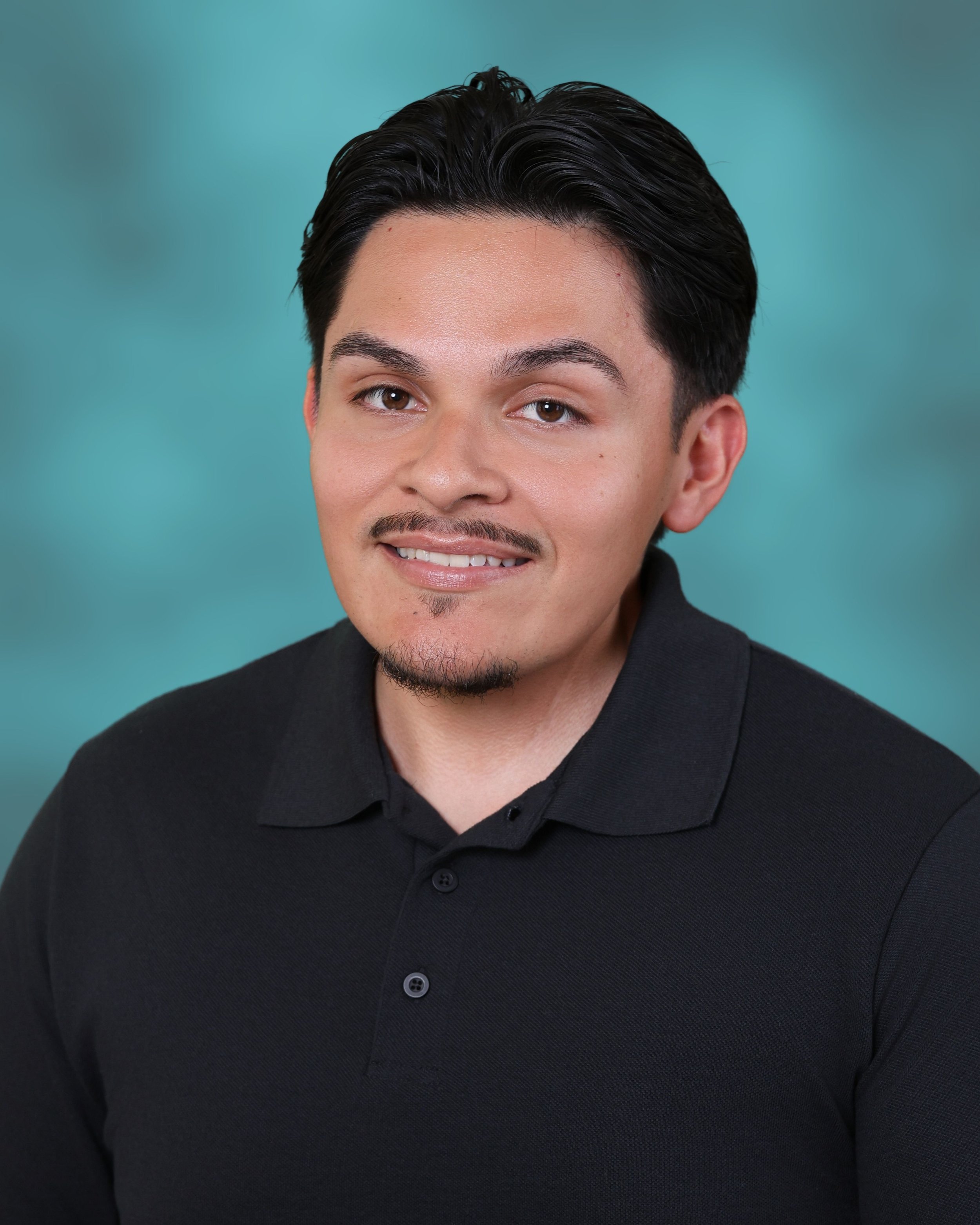 A young man with dark hair and brown eyes, smiling slightly, wearing a black collared shirt.