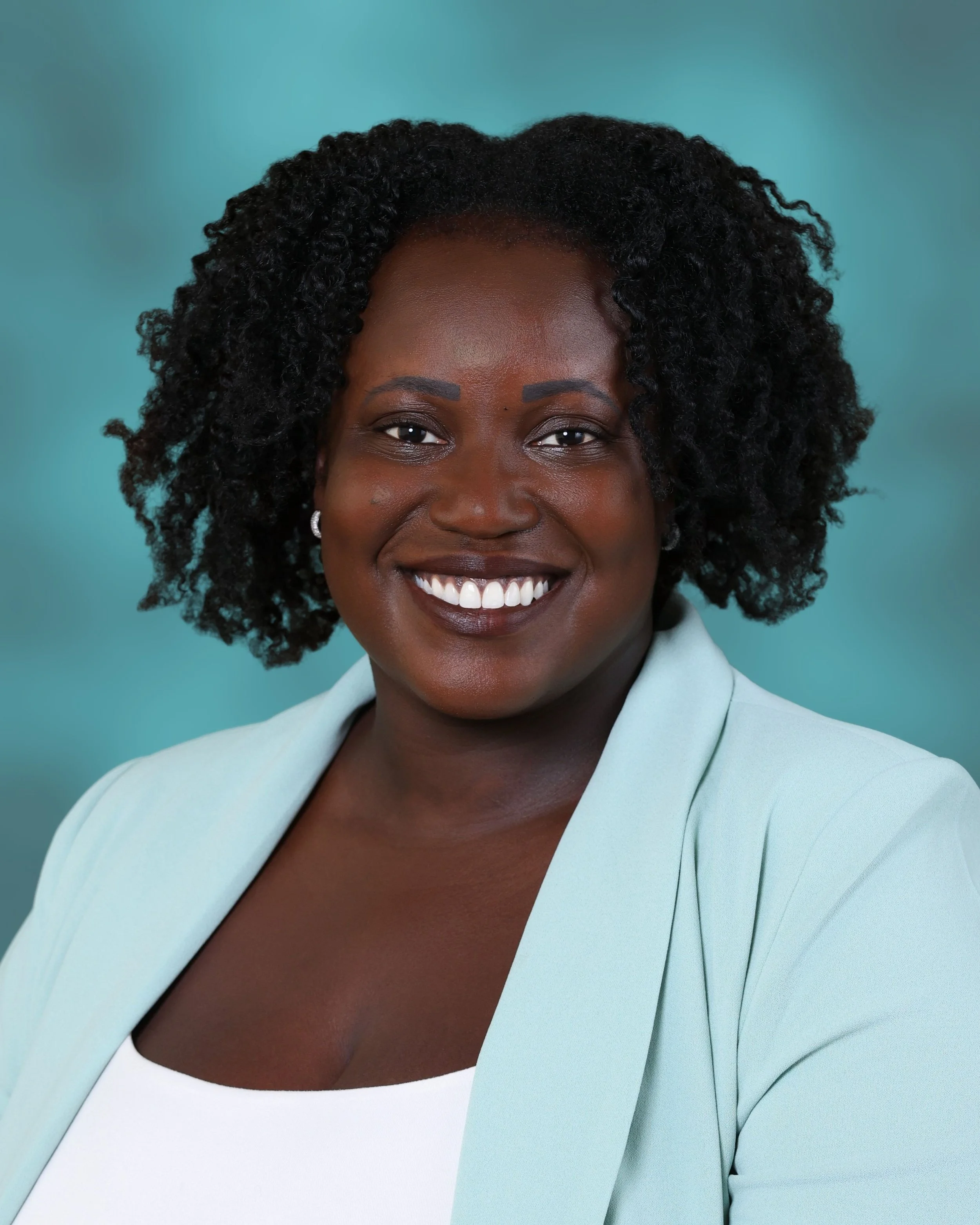Close-up of a woman with a bright smile, wearing a light blue blazer over a white top, against a teal background.